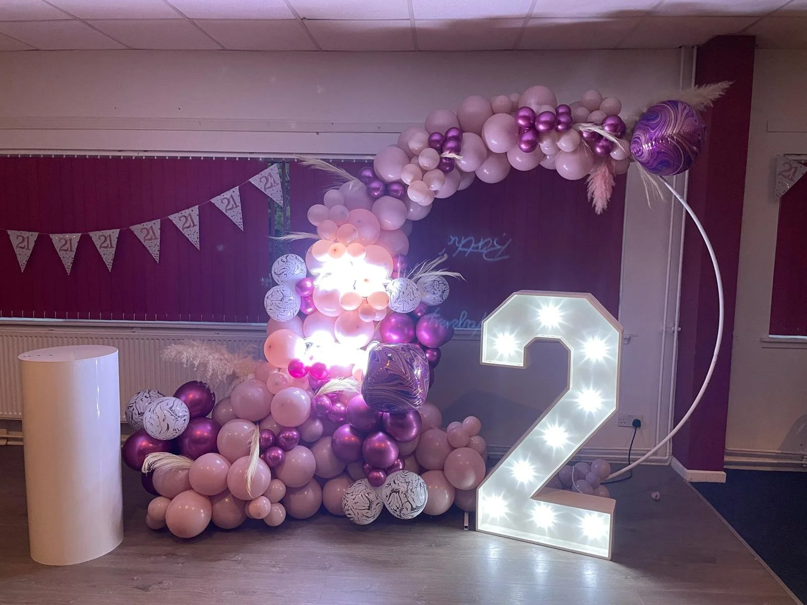 Decorative balloon arch with pink and purple balloons, white feathers, and decorative elements, and a lit-up number 2 for a celebration or birthday party.