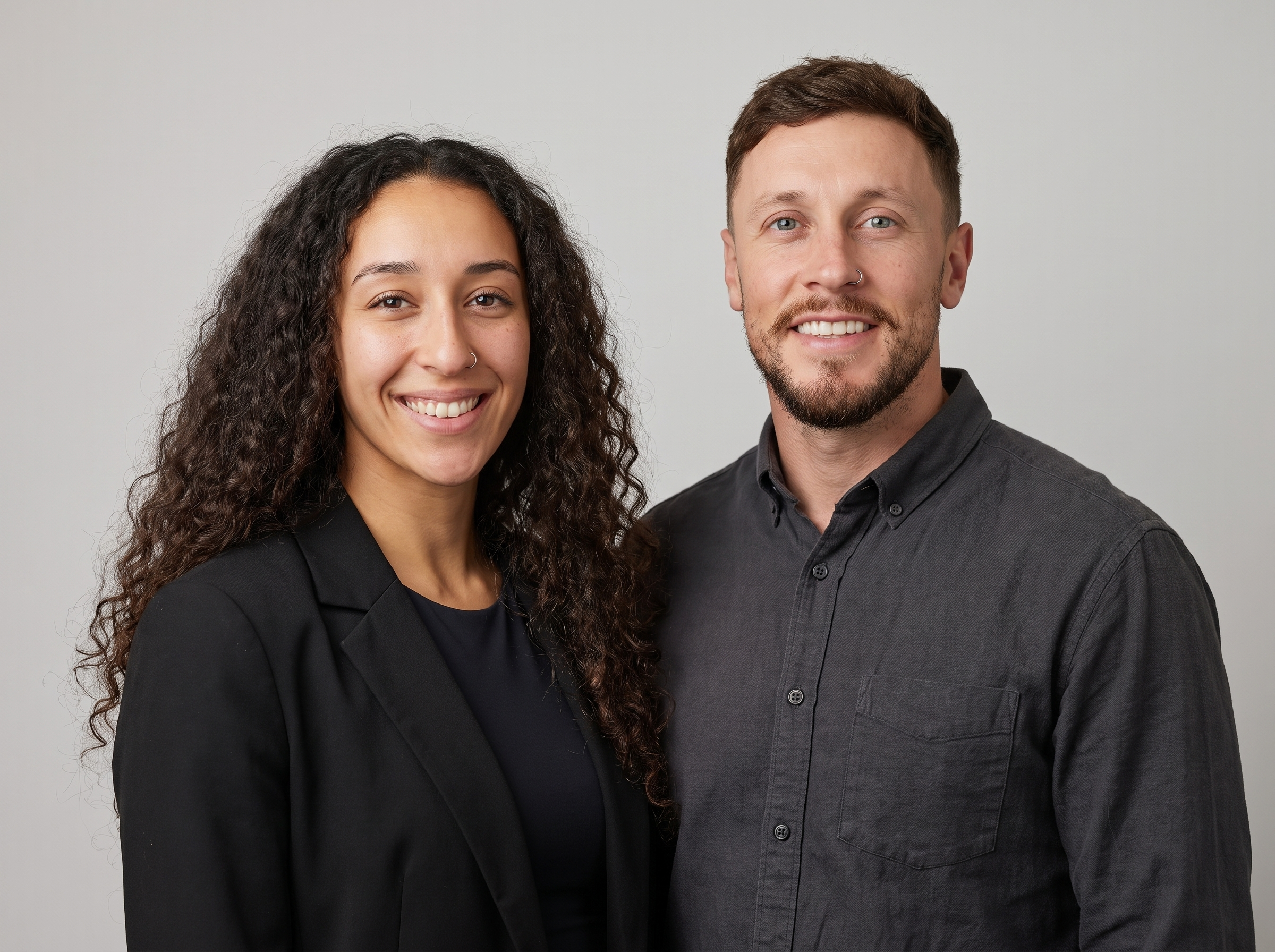 A woman and a man smiling and taking a selfie together against a plain light gray background.