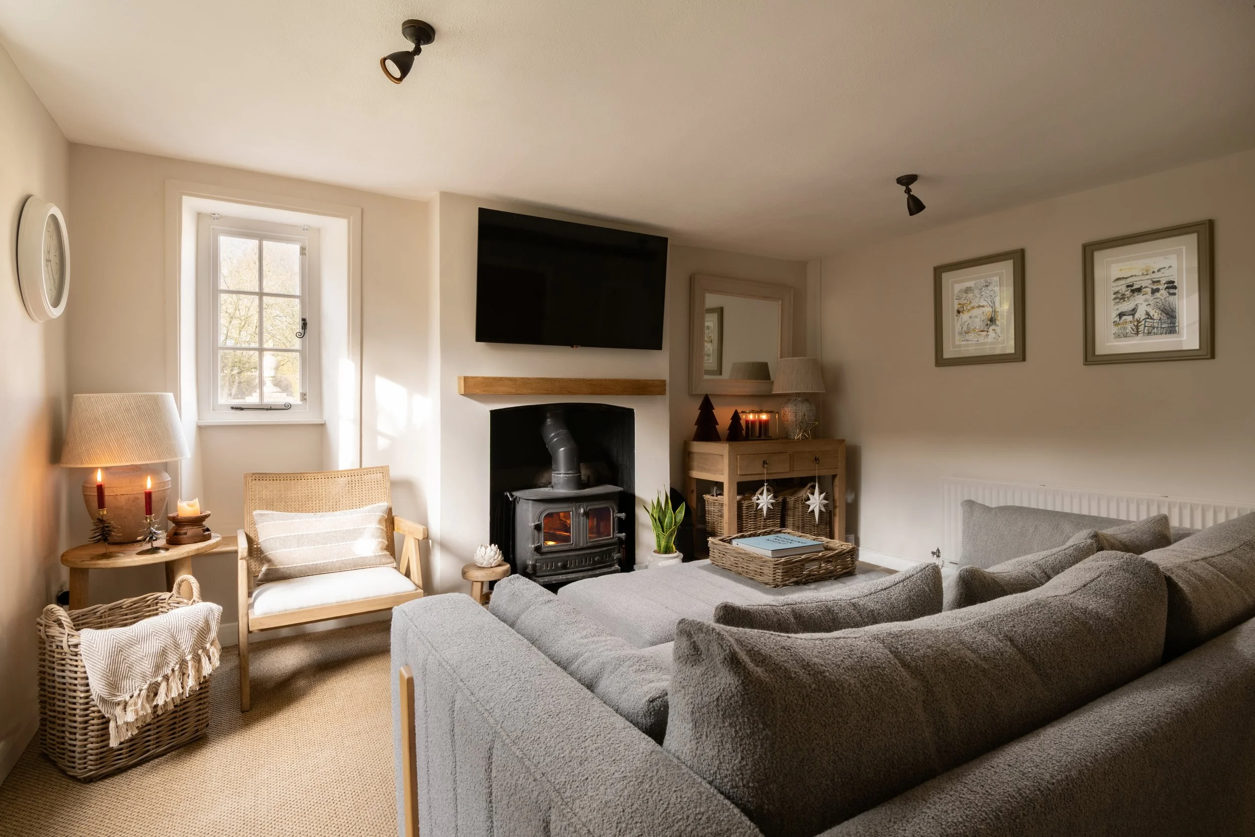 Living room with a gray sofa, wicker chair, wooden side table with candles, a fireplace with a TV above it, wall art, window with natural light, and various decorative items.