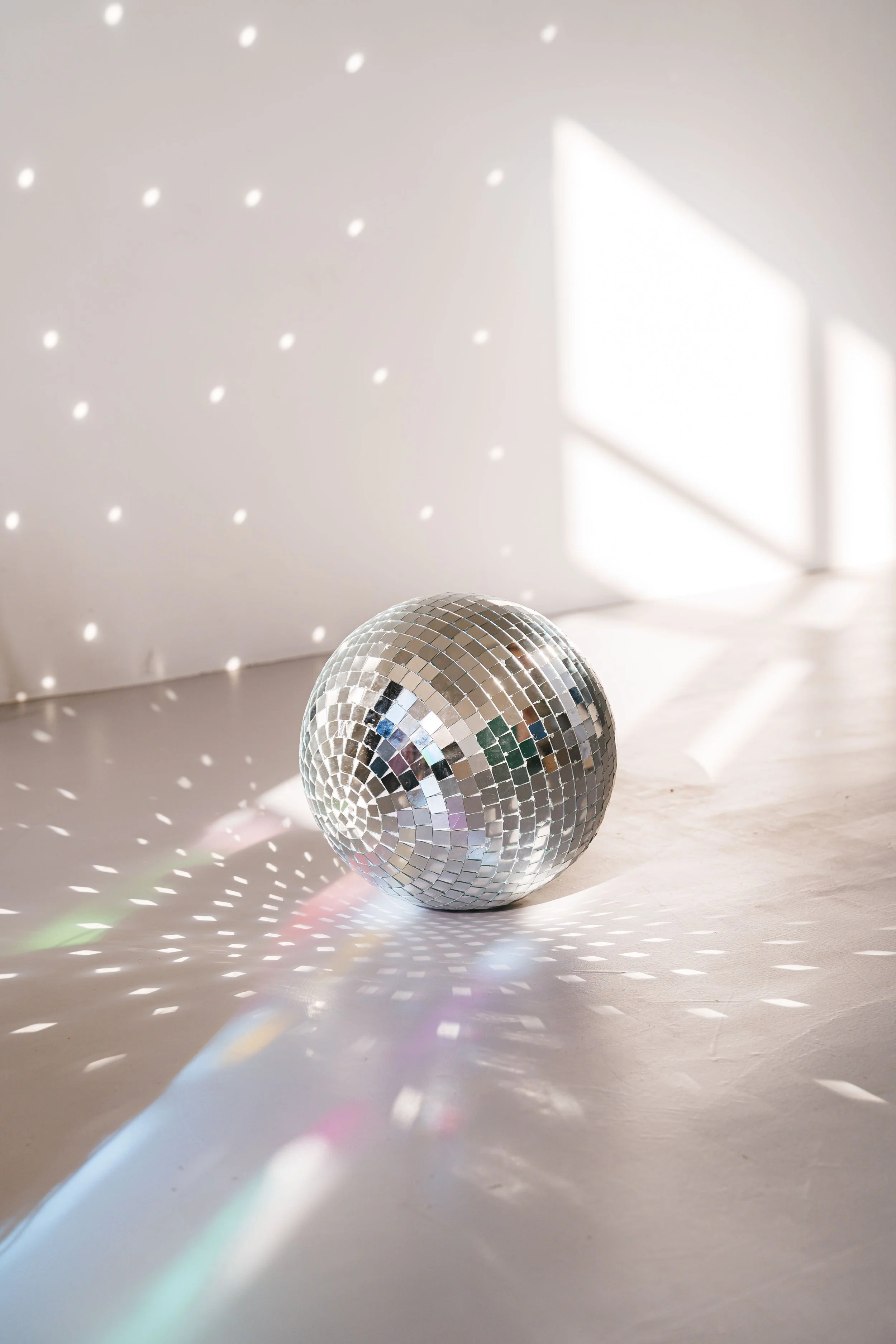 A disco ball with mirrored tiles reflecting light, creating a pattern of light spots on the white surface and wall in the background.