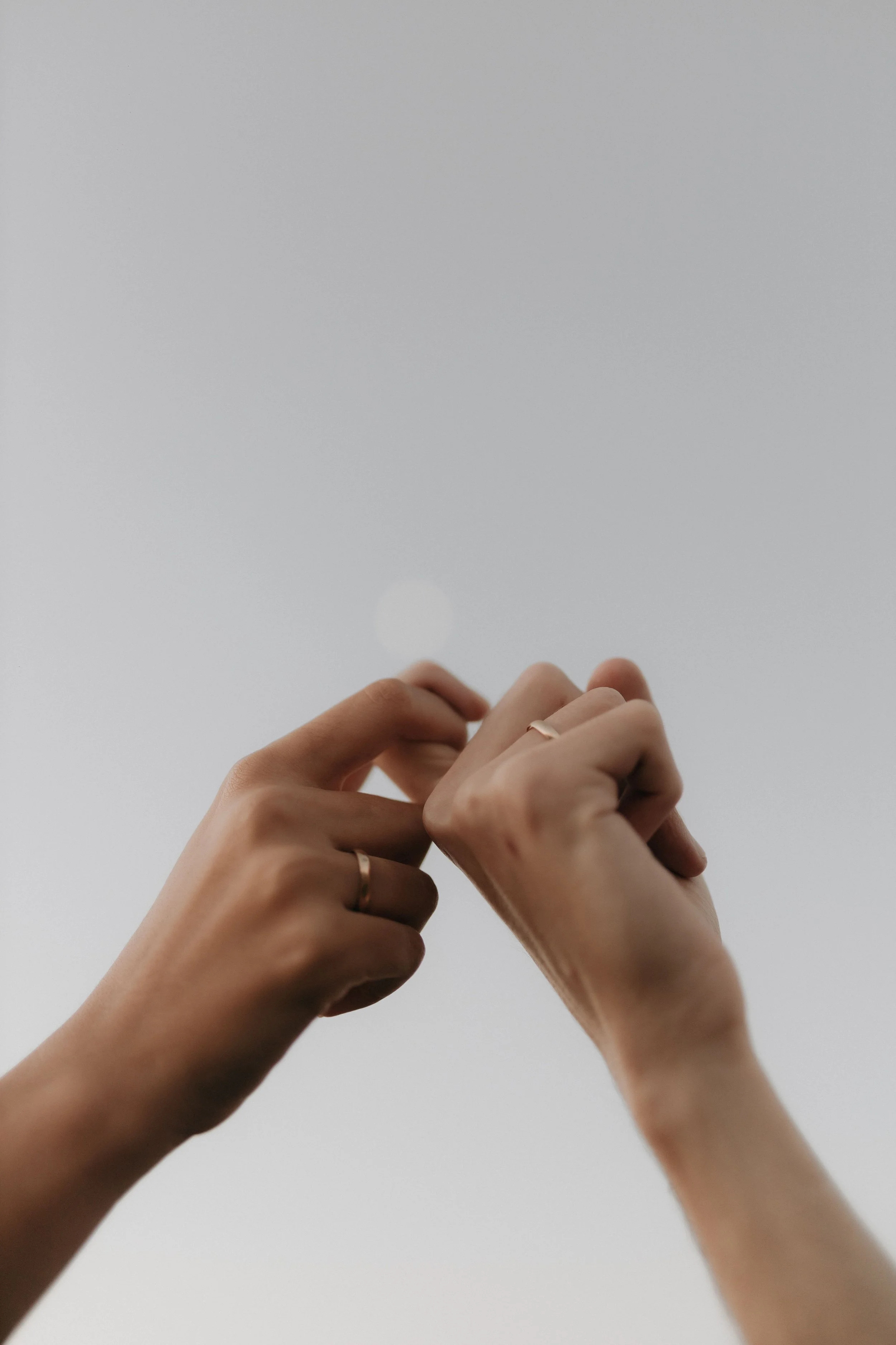 Close-up of human hands with rings, gently holding or touching each other against a plain white background.