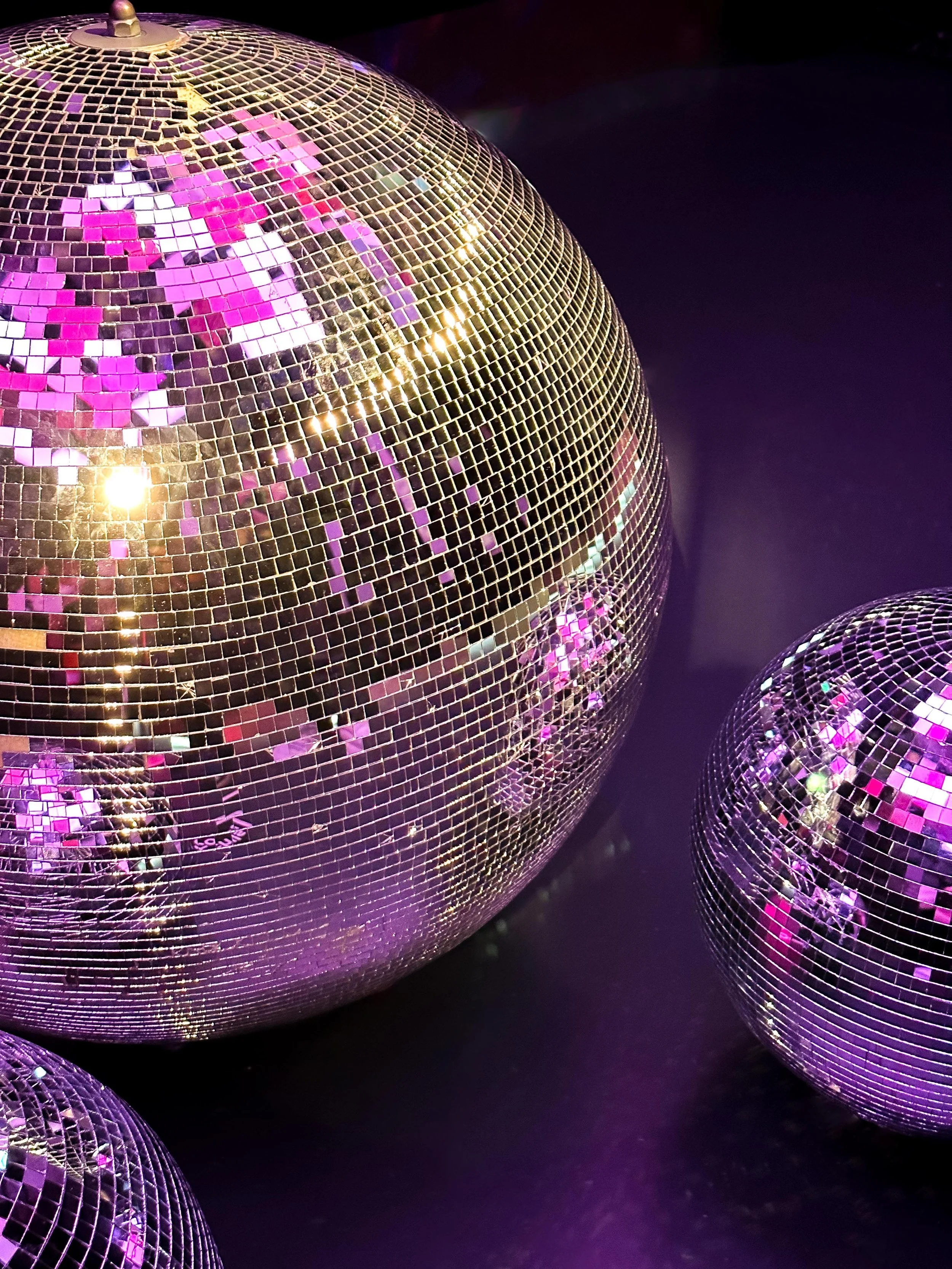 Close-up photo of disco balls with reflective mirrors, emitting purple and pink lights against a black background.