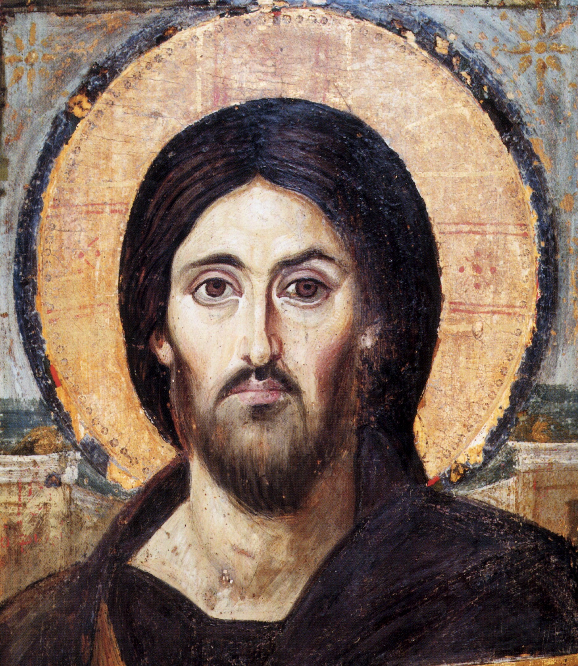 Close-up of an ancient Christian Orthodox icon painting of Jesus Christ with dark hair, a beard, and a halo, painted on wood with a weathered surface.