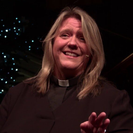 A woman dressed as a priest smiling and waving