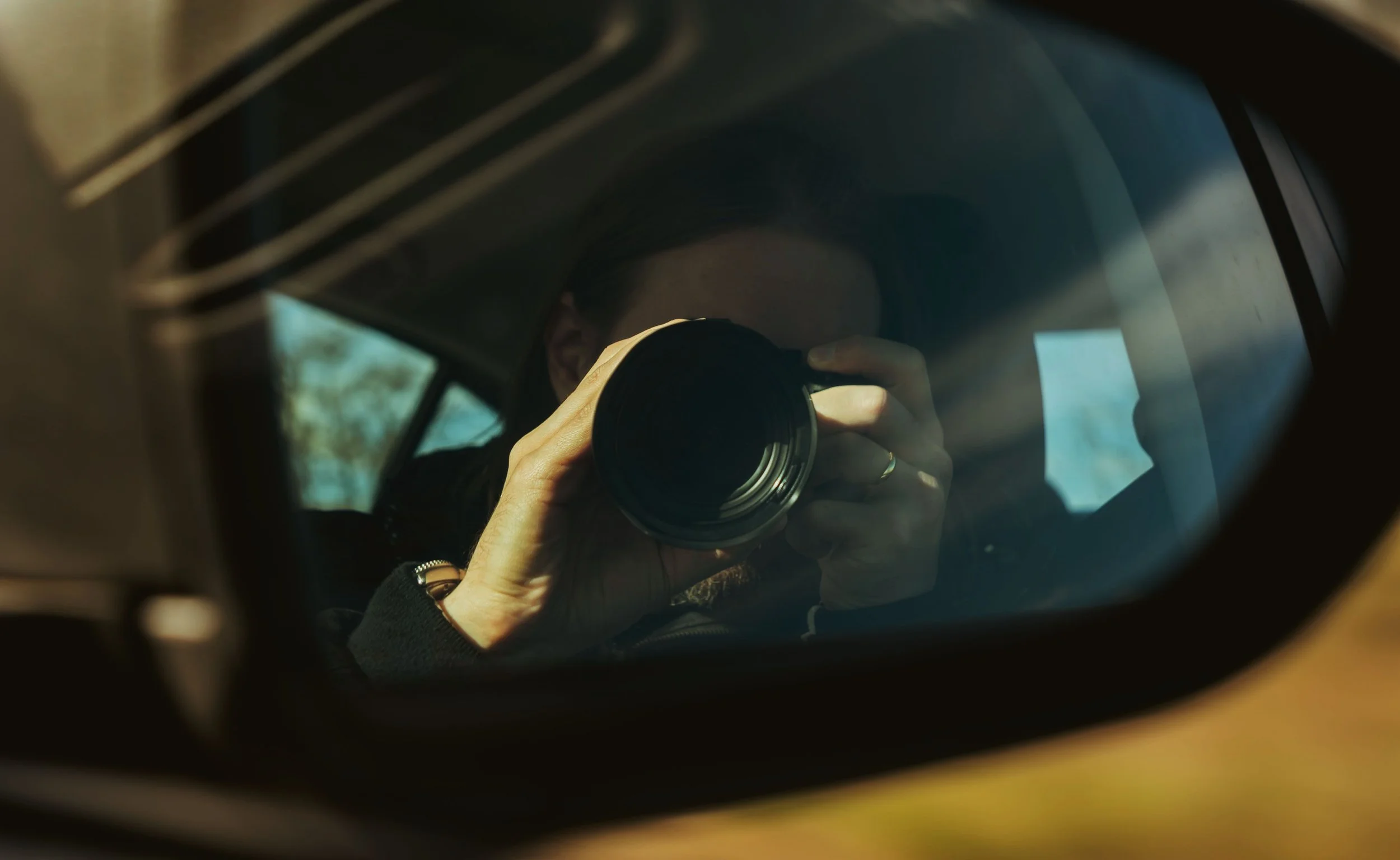 Person taking a photo with a camera, reflected in a car mirror.