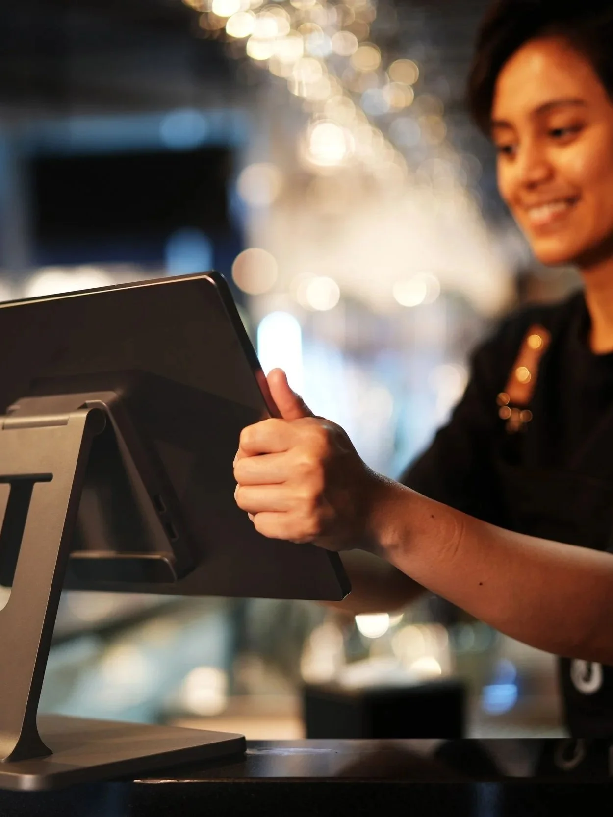 A woman smiling as she interacts with a tablet device at a counter in a well-lit indoor space.