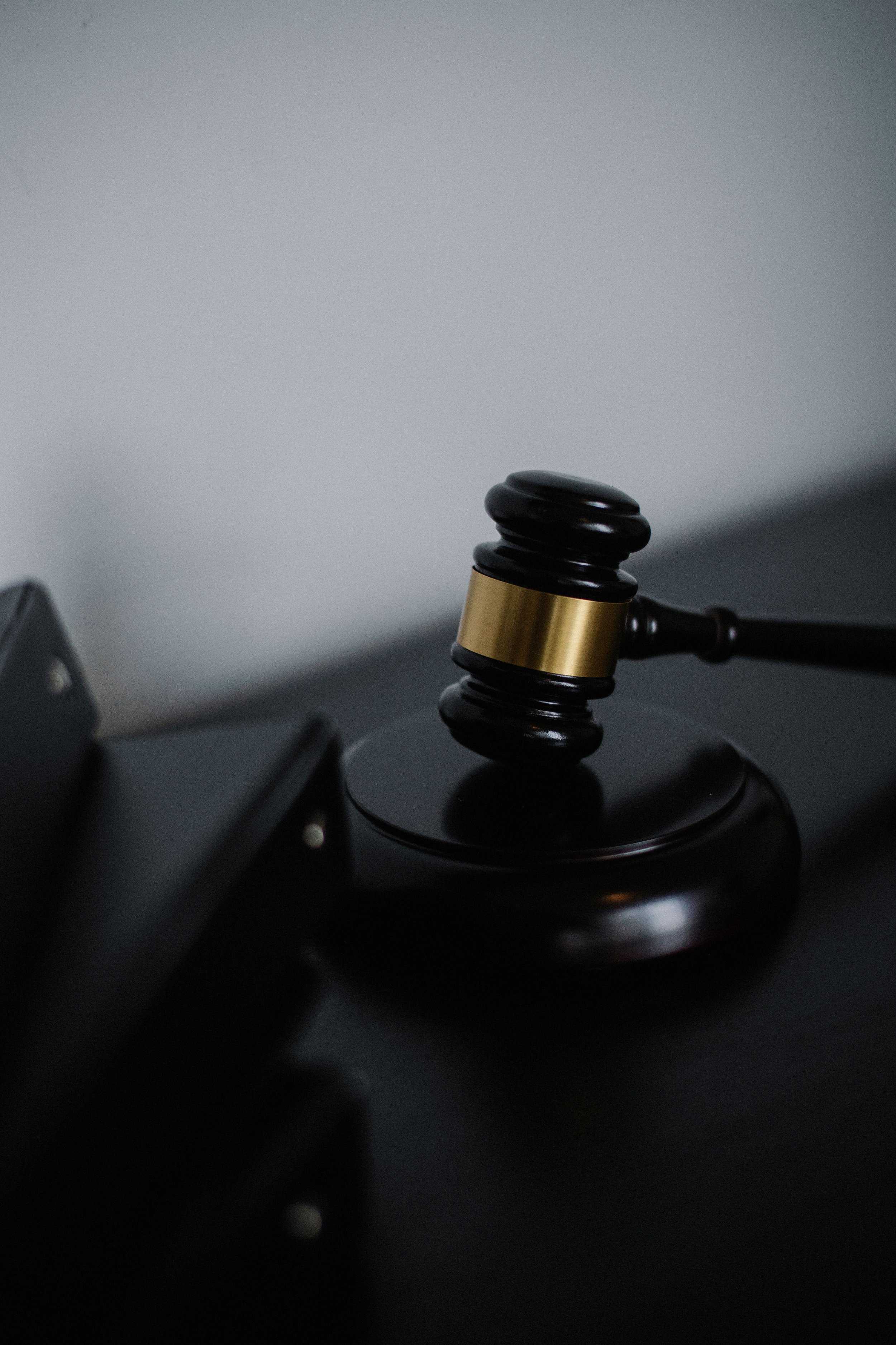 Close-up of a judge's gavel resting on a sound block, with surrounding blurred objects.