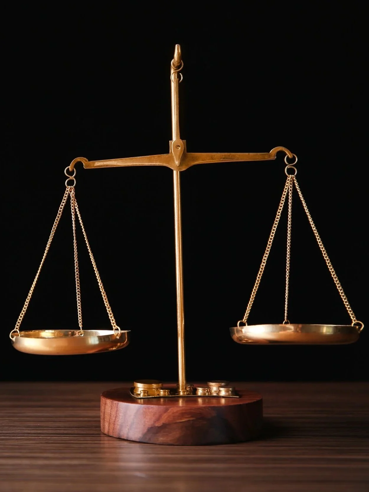 Gold balancing scale on a wooden base with coins below, against a black background.