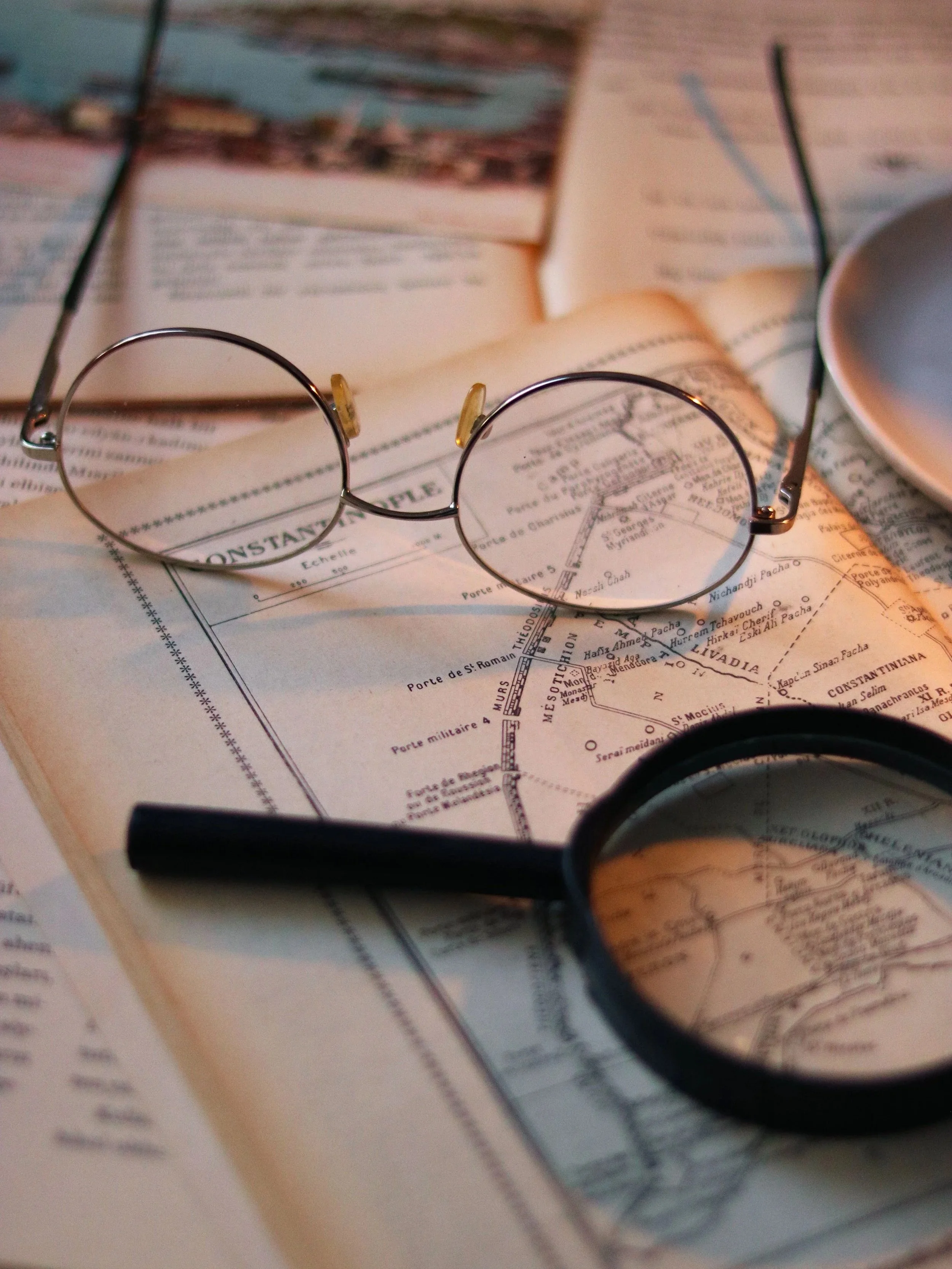 Close-up of eyeglasses resting on an open book or map, with other books in the background.
