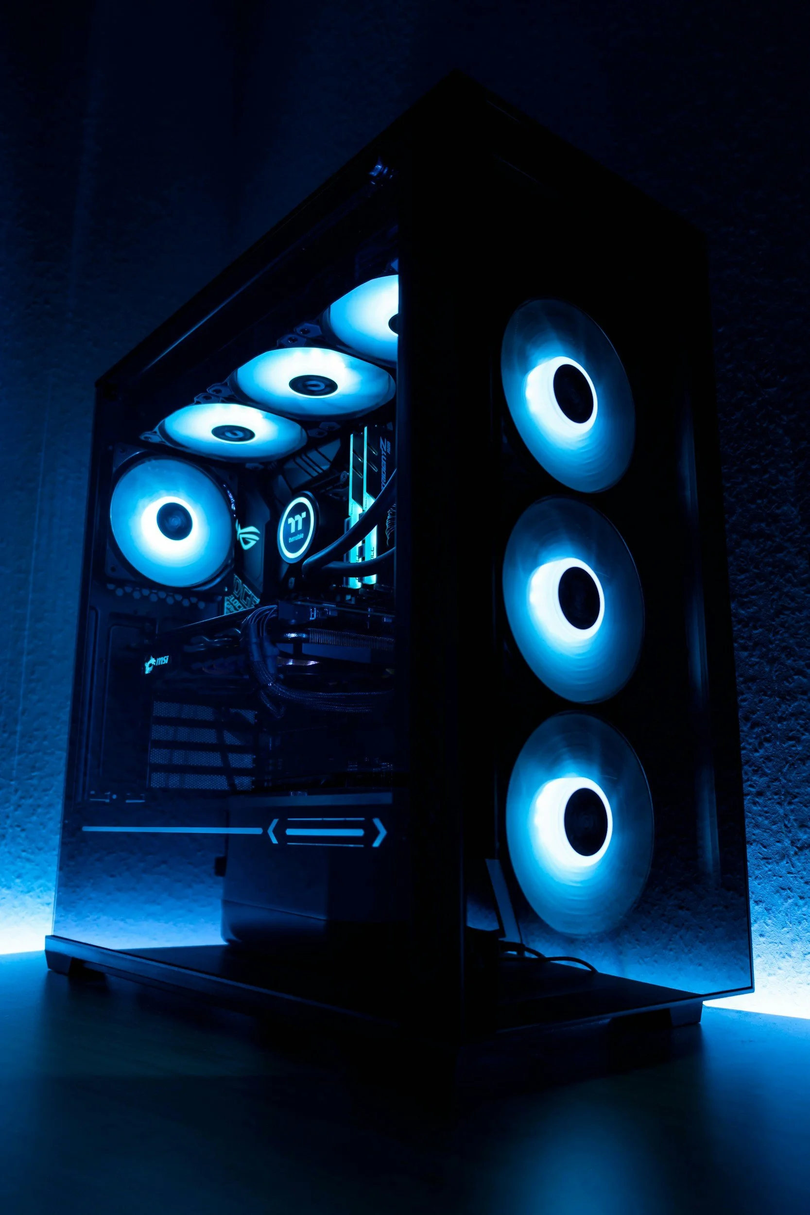 A gaming computer with illuminated fans inside a transparent case, with a blue LED lighting effect.