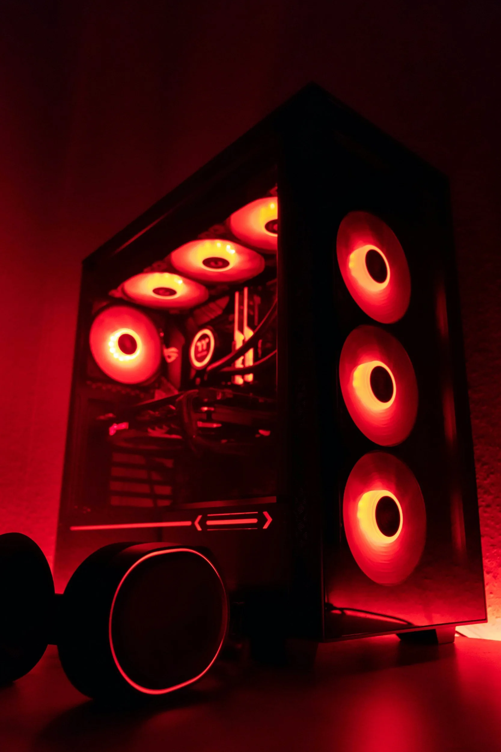 A gaming computer with red LED lights inside a case glowing through multiple side windows, placed on a black surface in a dark room.