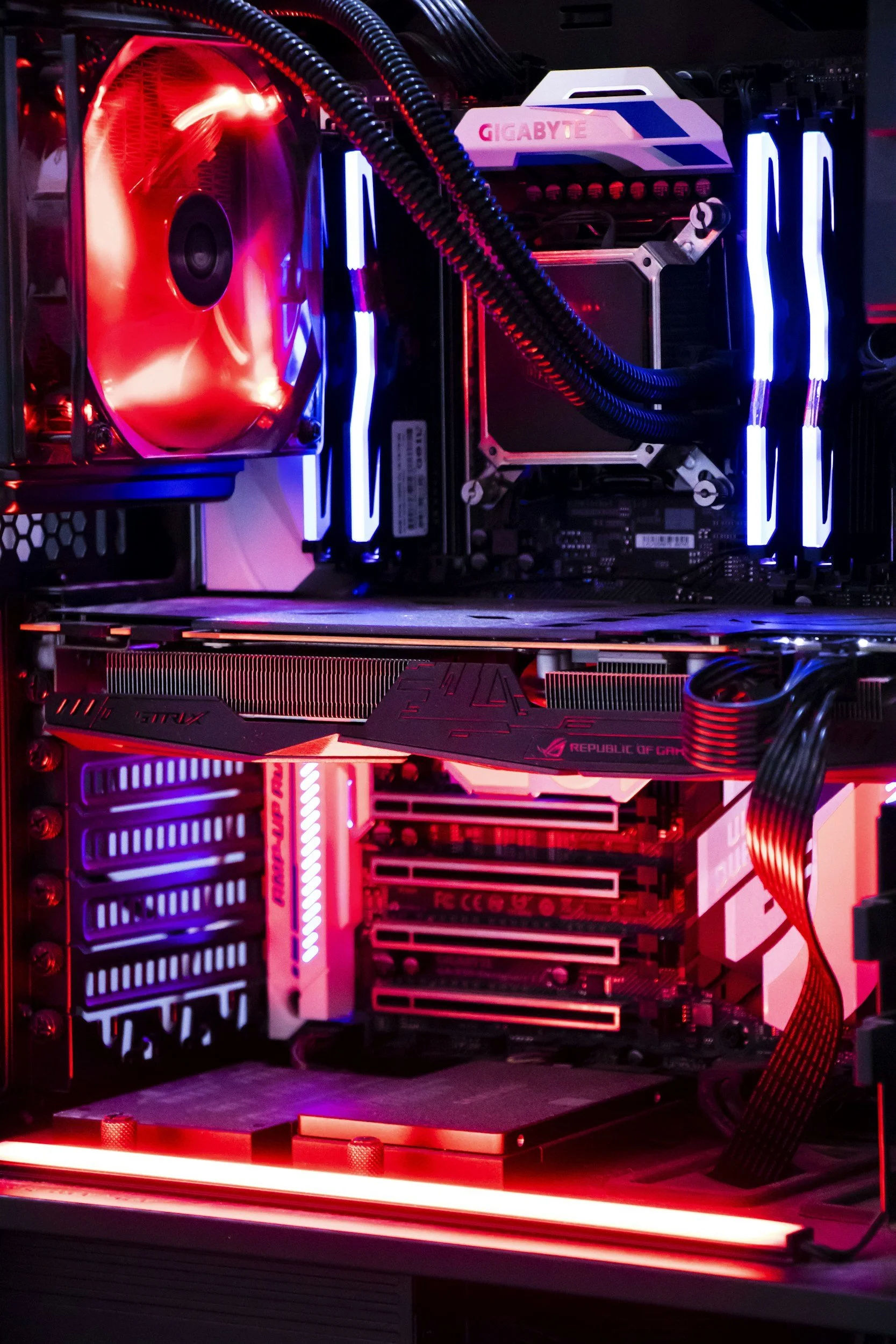 A desktop computer interior with a large illuminated cooling fan, LED lighting, and various computer components including a Gigabyte motherboard and graphics card, all lit with red and blue lighting.