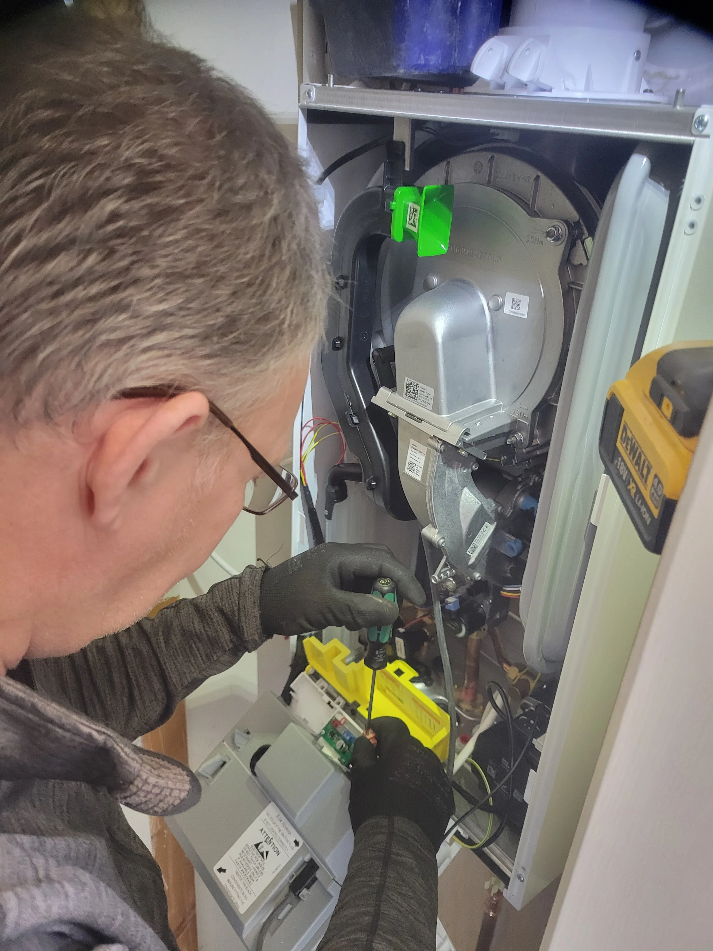 A person working on an electrical panel or circuit breaker box, using a screwdriver, inside a building.