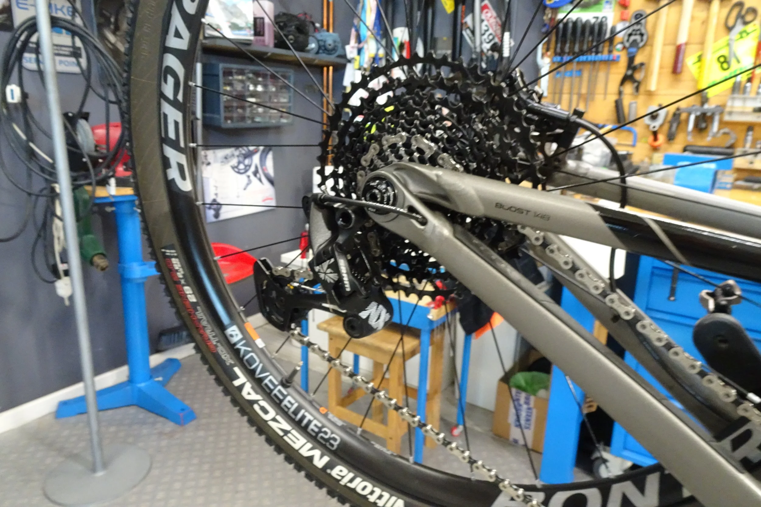 Una bicicletta da mountain biking in un’officina, con vari strumenti e pezzi di ricambio sullo sfondo.