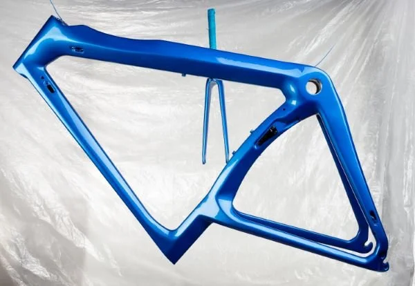 Blue bicycle frame hanging in front of a white background.