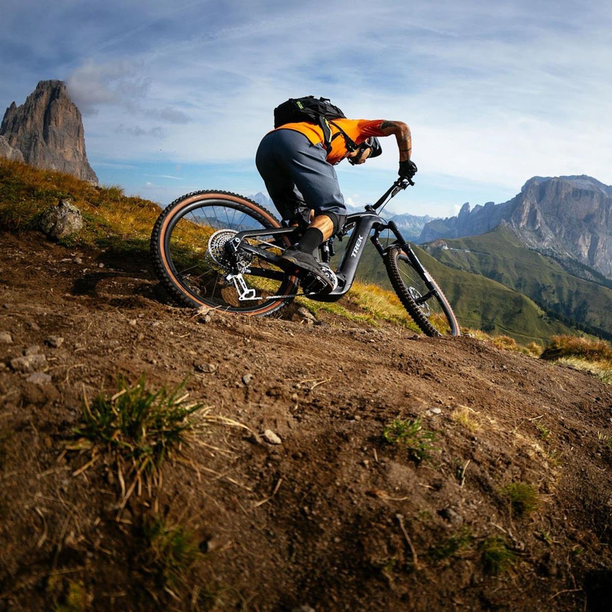 Un uomo in mountain bike rovesciato su un sentiero di montagna, con uno scenario di montagne e cielo azzurro sullo sfondo.