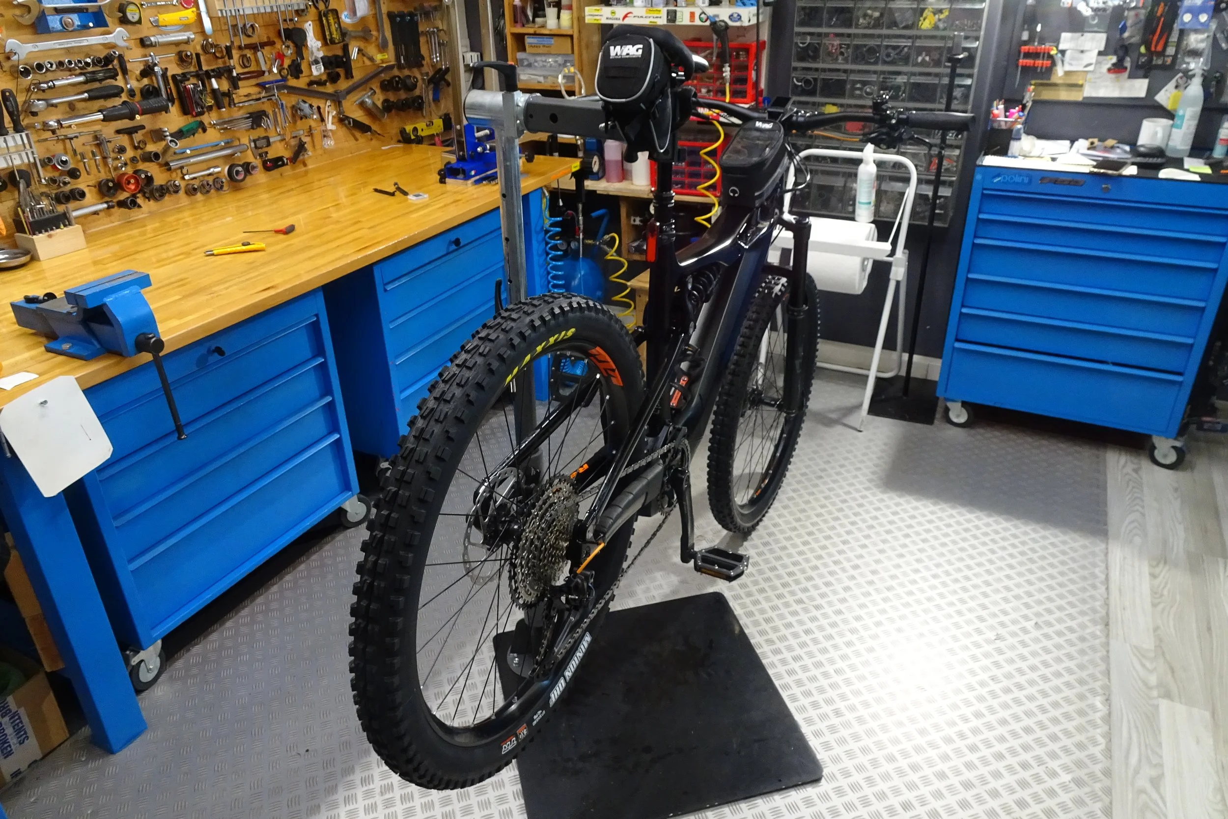 Bici da mountain bike di fronte a un banco da lavoro in officina, con utensili e arnesi appesi alla parete, in un ambiente di falegnameria o riparazione.