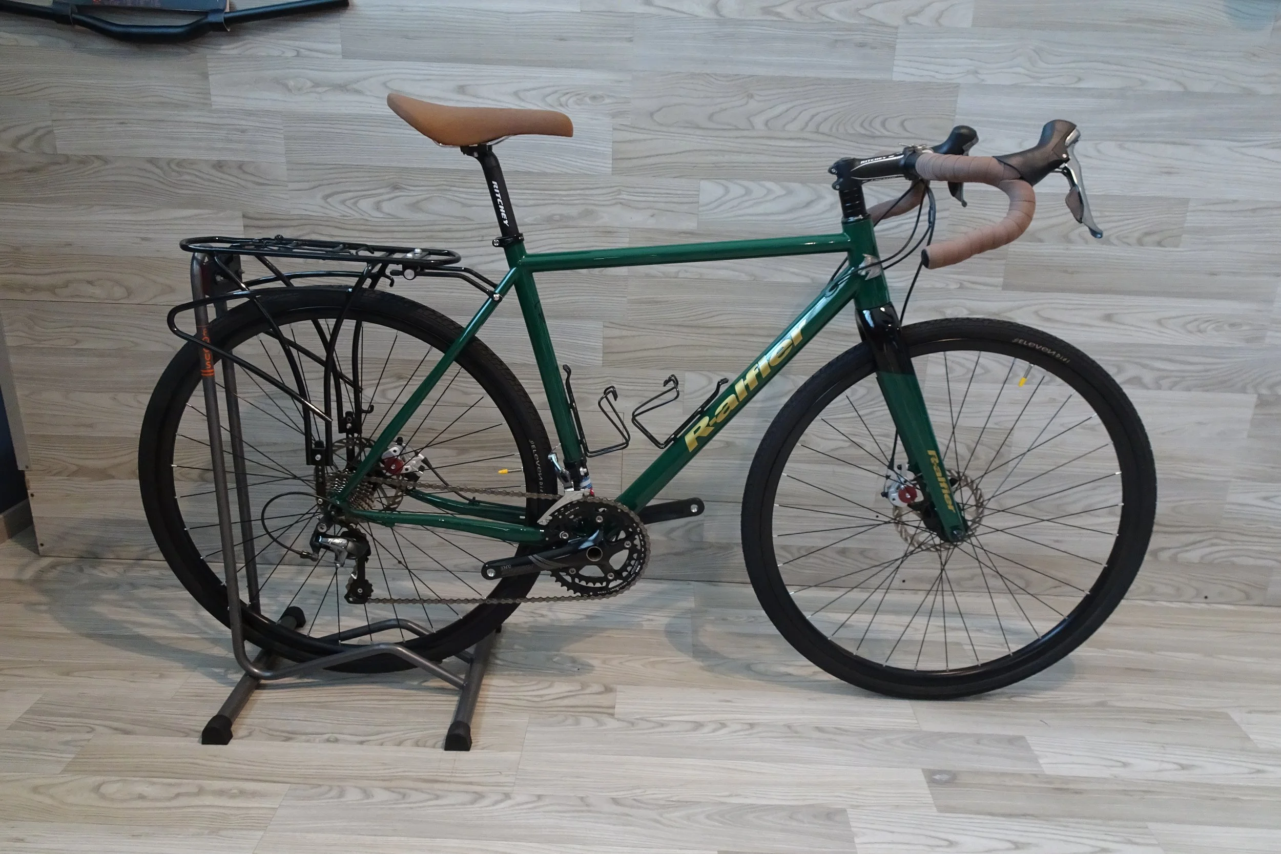 Bicicletta green con sensori di freno e manubrio con copertura marrone, posizionata su un supporto all'interno su un pavimento in legno chiaro.