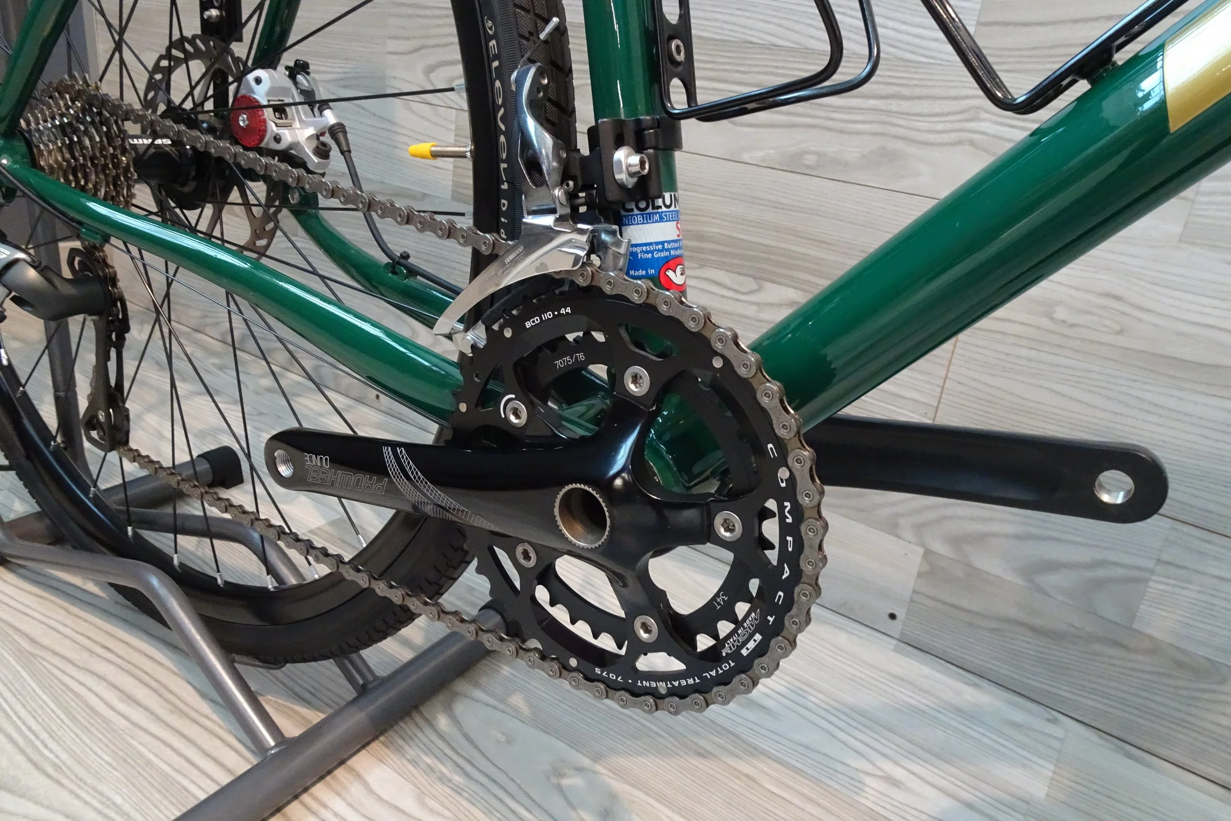 Partita di bicicletta con dettaglio del telaio, trasmissione, catena, corona e deragliatore, tutto su una superficie in legno.