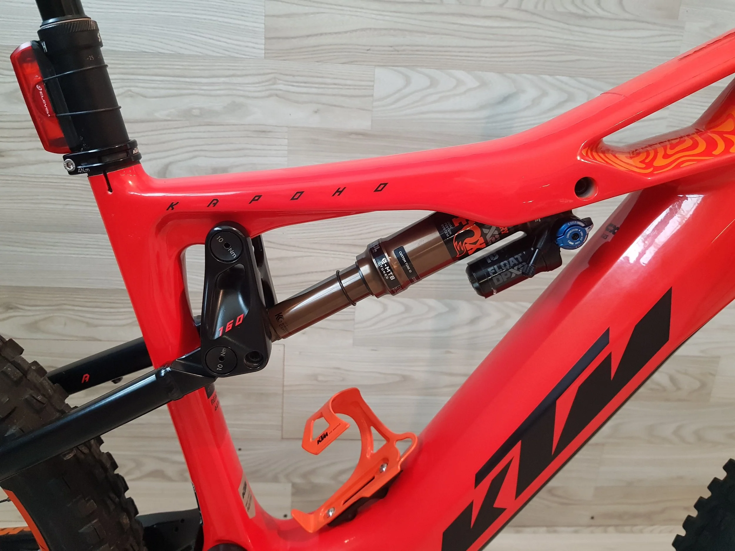 Bicicletta da mountain bike di colore rosso con sospensioni e componenti di alta qualità, posizionata su un pavimento di legno chiaro.