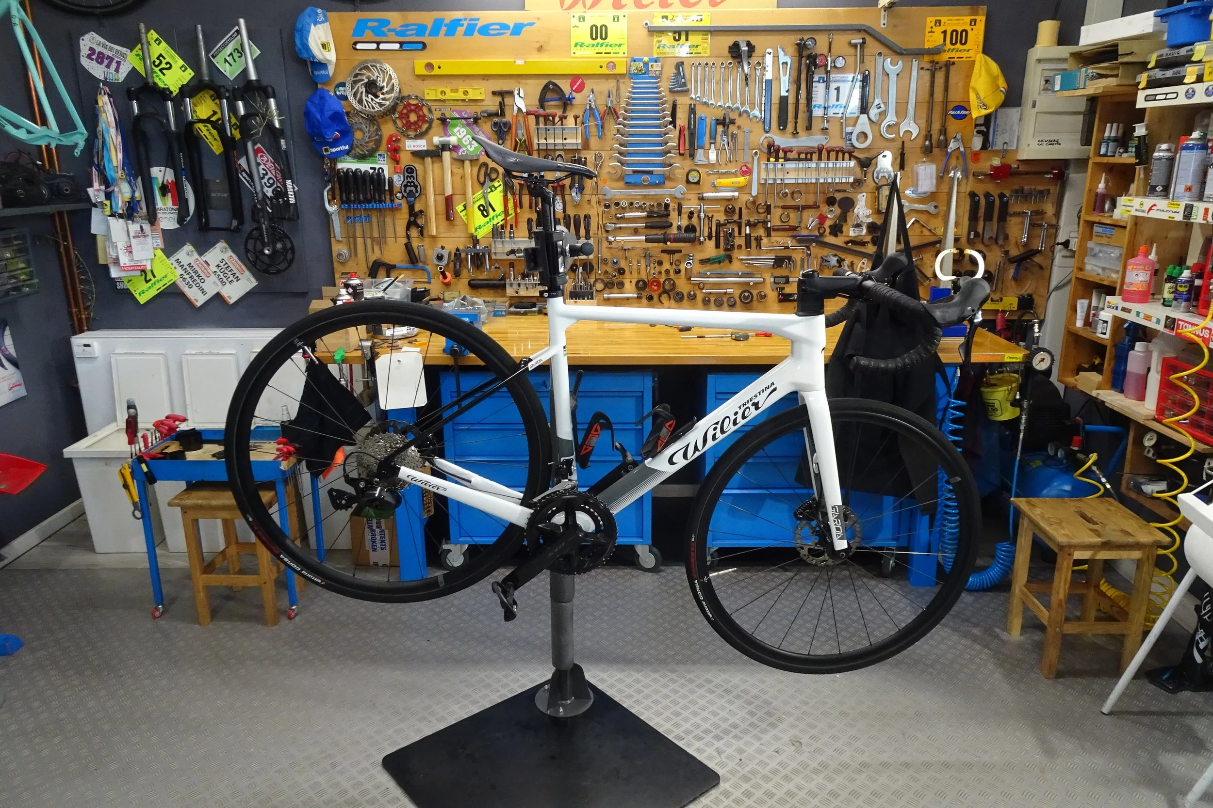 Bicicletta da corsa bianca posizionata davanti a un banco da lavoro con attrezzi e strumenti per la riparazione delle biciclette, in un'officina.