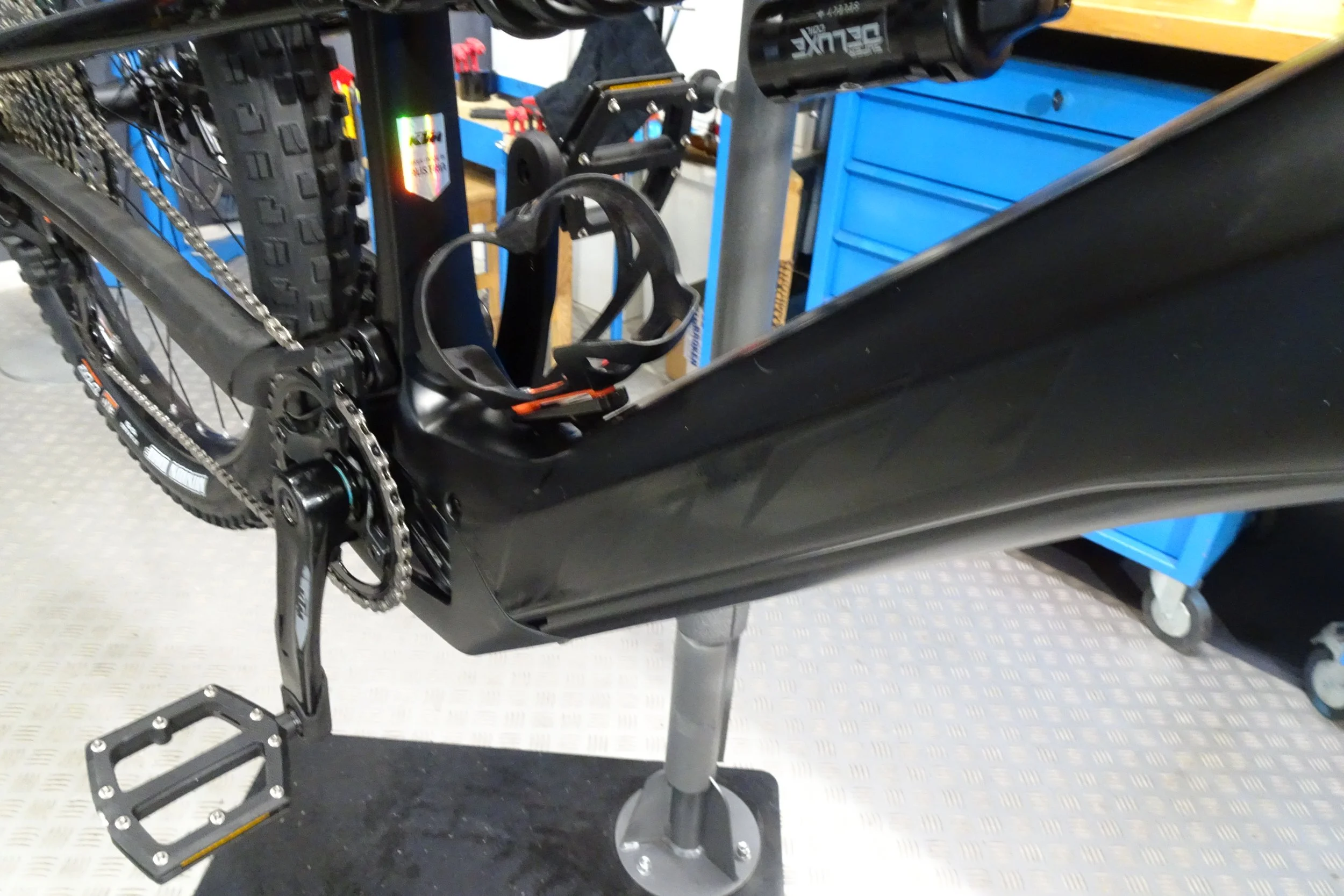 Parti di una mountain bike, inclusi il telaio, la catena, i pedali e i componenti del cambio, appoggiata su un supporto in un laboratorio o officina.