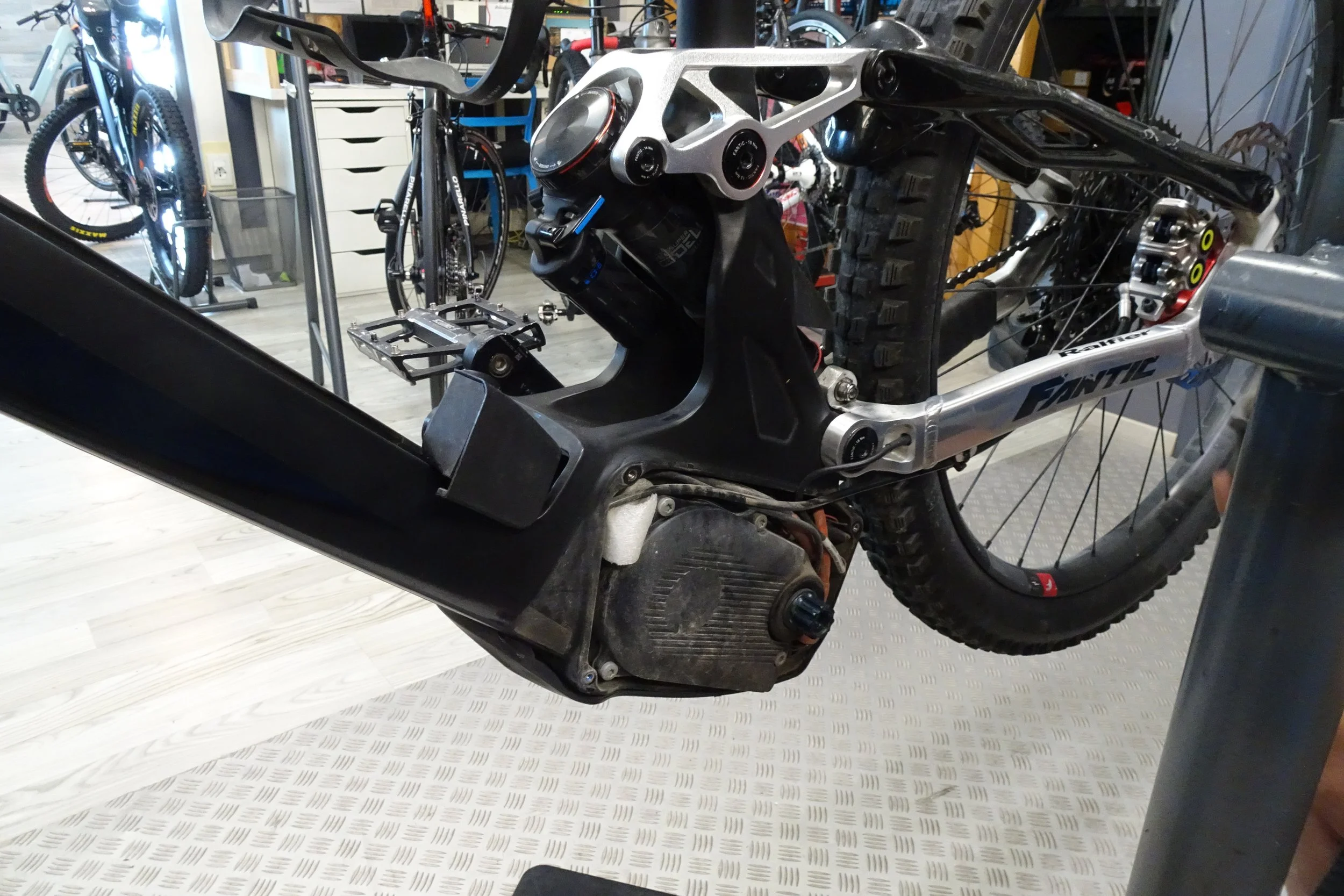 Immagine di una bicicletta da mountain bike in fase di riparazione o manutenzione, con il telaio smontato e componenti come il motore e la sospensione visibili, in un'officina o un laboratorio.