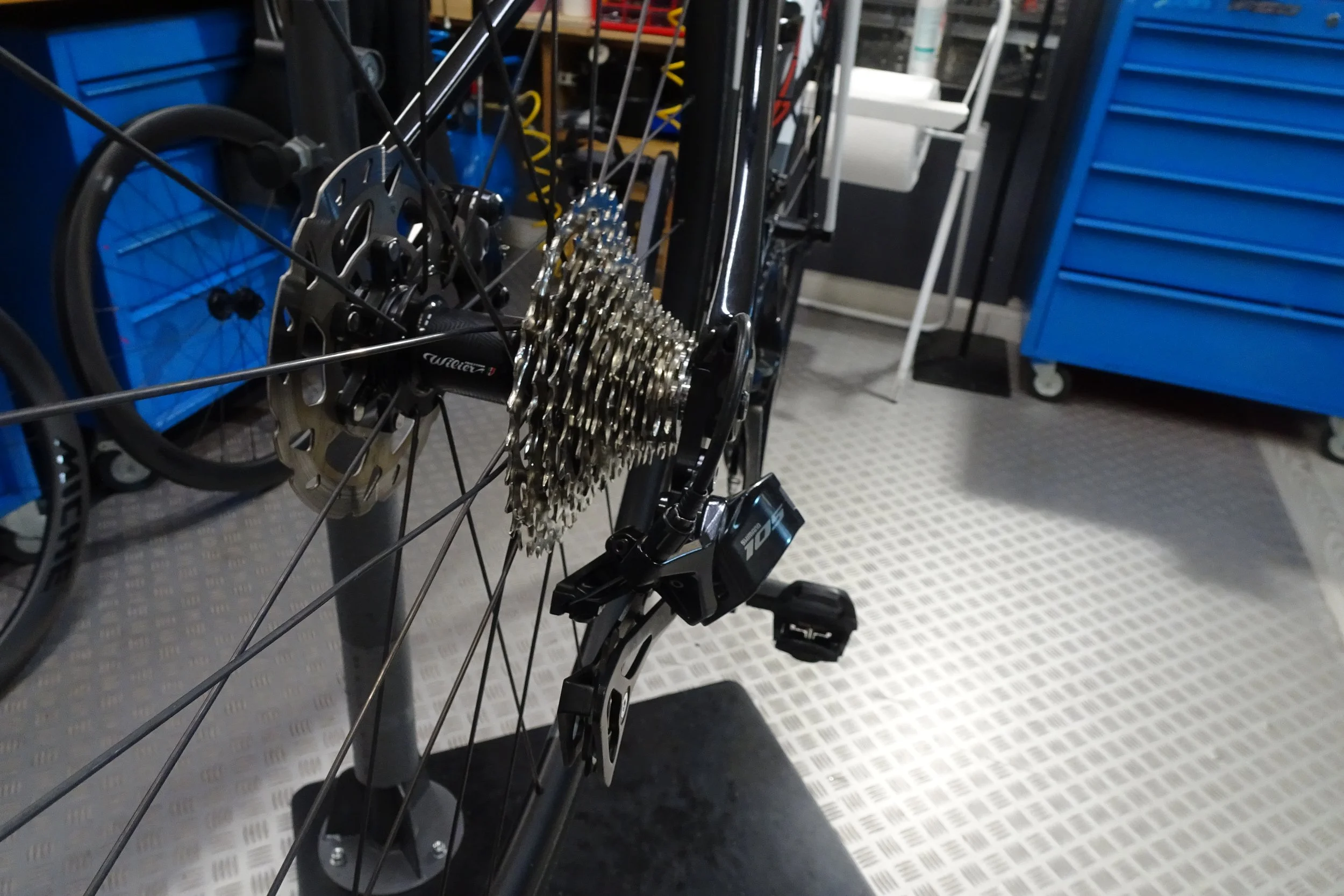 Ruota di bicicletta con cambio e leve freno in un garage con strumenti e scaffali blu.