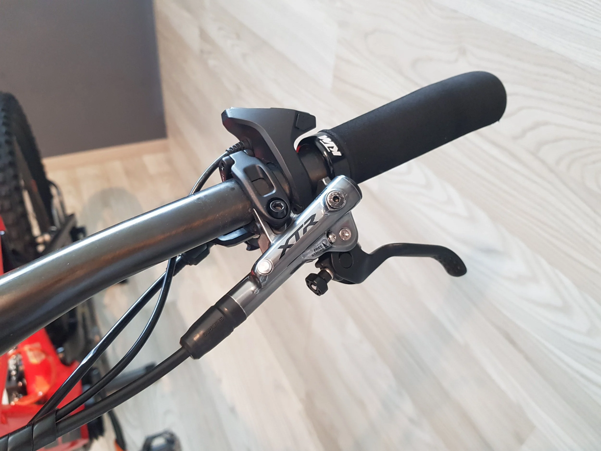 Manubrio di una mountain bike con manopola nera, freno e componenti meccanici visibili.