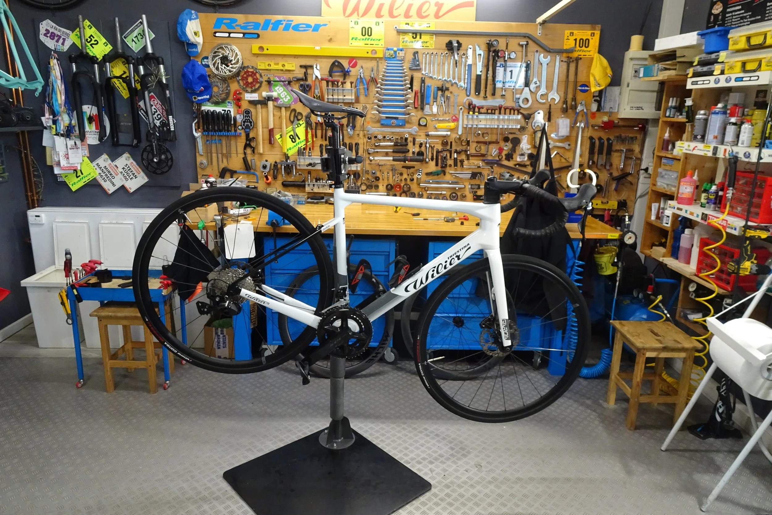 Un negozio di riparazioni di biciclette con utensili e attrezzi appesi alle pareti e una bici da corsa in primo piano.