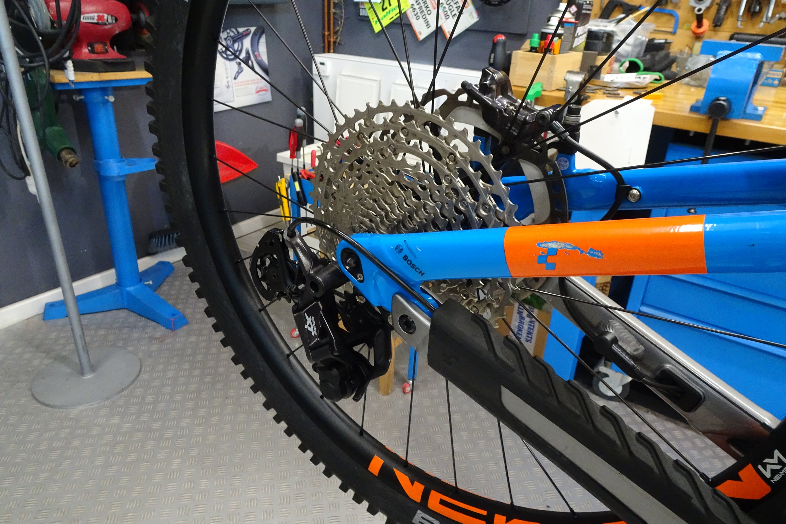 Ruota di bicicletta da montagna con cambio e pignoni, in un'officina con attrezzi e mazze appoggiate.