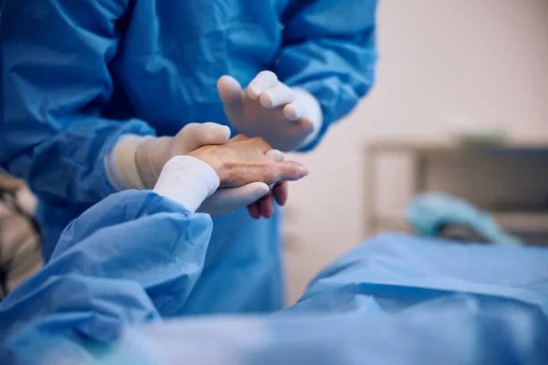 Healthcare professional comforting a patient by holding their hand in a hospital room.