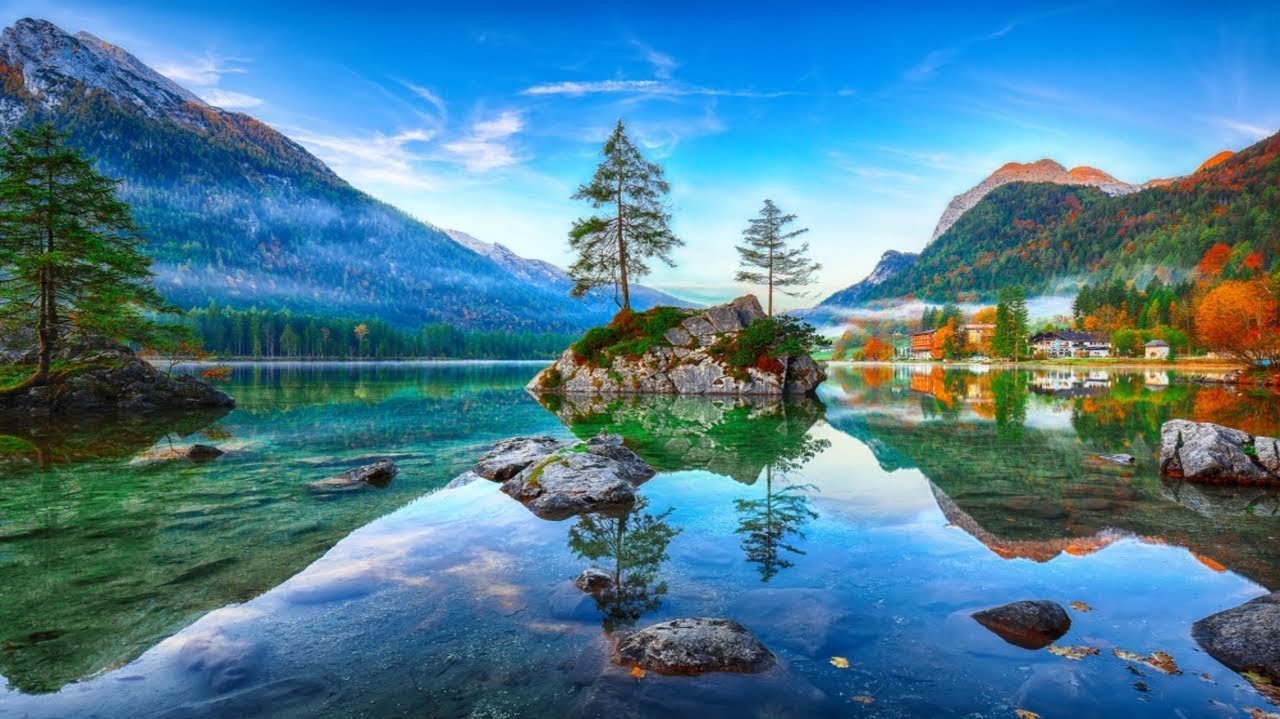 Calm mountain lake surrounded by trees and mountains, reflecting the sky and landscape.