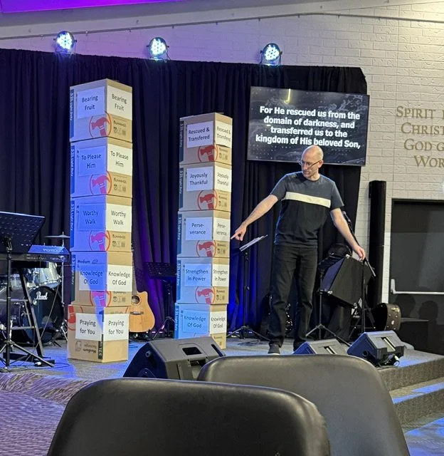Pastor Kevin Dunn is preaching a sermon at Gympie Church of Christ with bunnings boxes in the background with signs illustrating the points of the sermon.