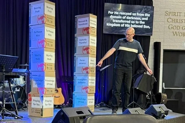 Pastor Kevin Dunn is preaching a sermon at Gympie Church of Christ with bunnings boxes in the background with signs illustrating the points of the sermon.