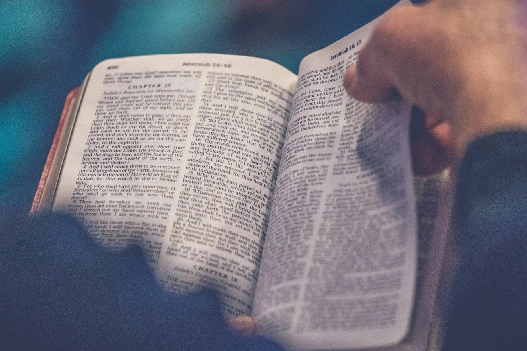 An open Bible showing pages with text from Jeremiah 16-17, held by a person's hand.