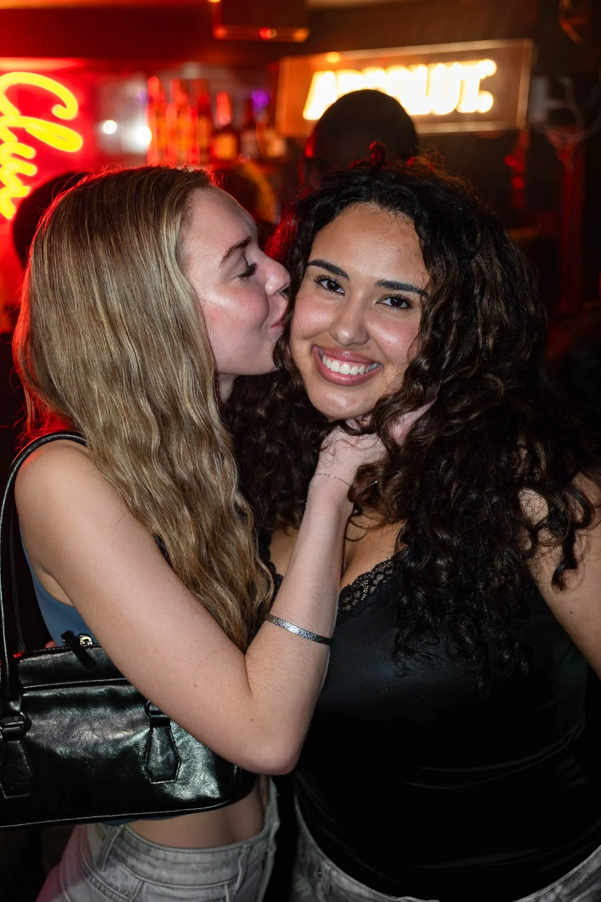 Twee jonge vrouwen die elkaar in een bar of club kussen, omringd door neonverlichting.