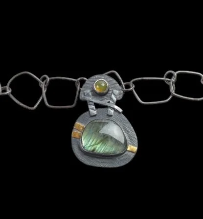 Close-up of a silver necklace with a round, greenish gemstone pendant on a black background.