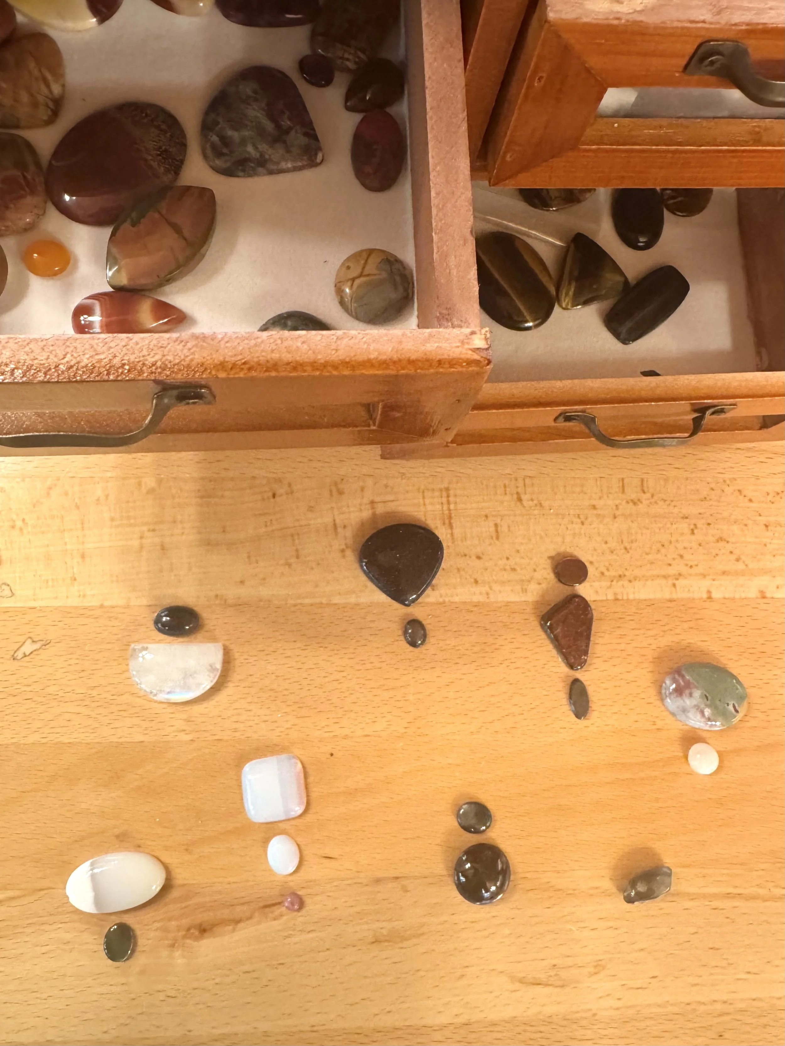 A wooden display case with a glass top containing various polished stones and gemstones of different colors, shapes, and sizes.
