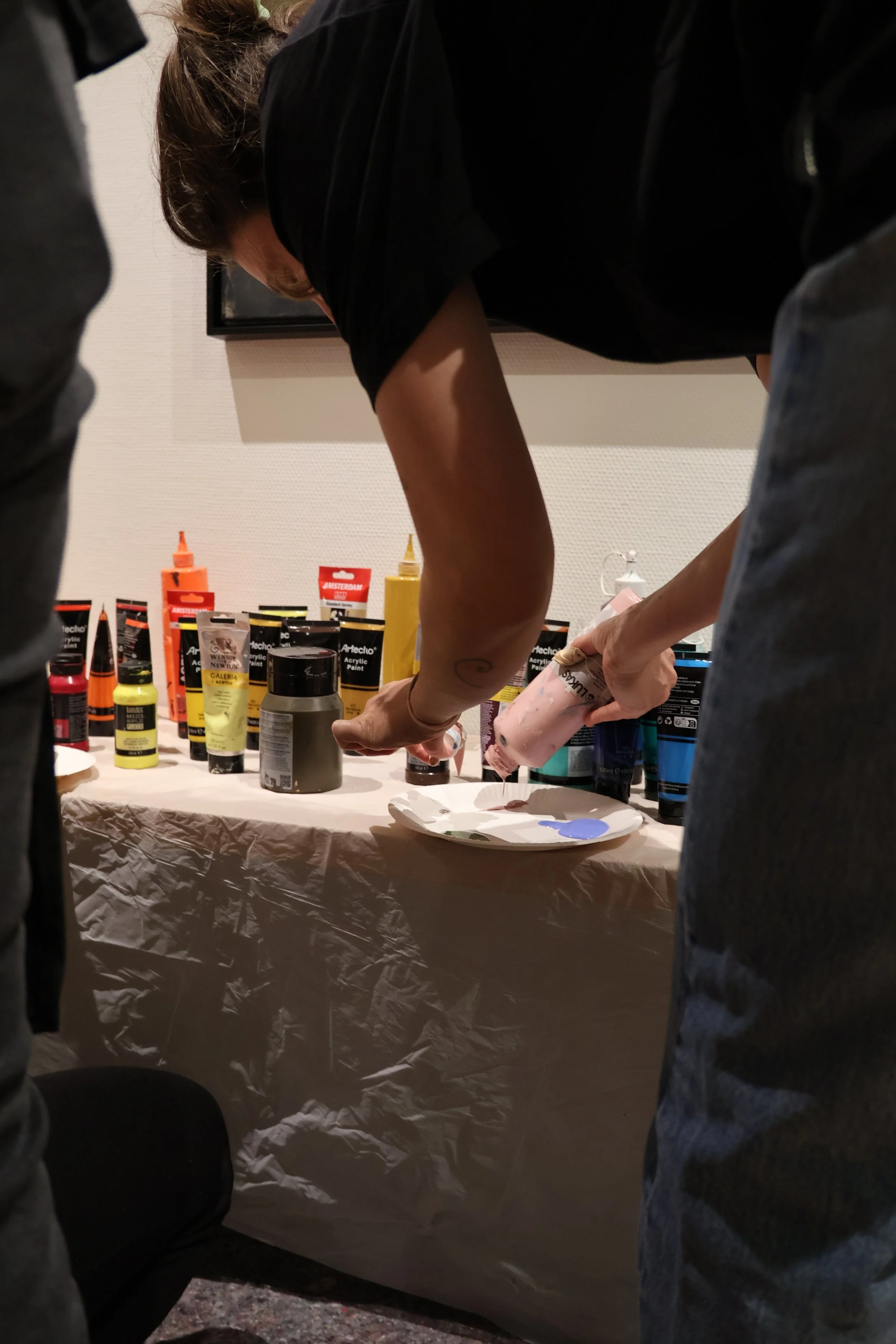 Menschen bei einer kreativen Aktivität, die auf einem Tisch mit verschiedenen Farben und Materialien arbeitet.
