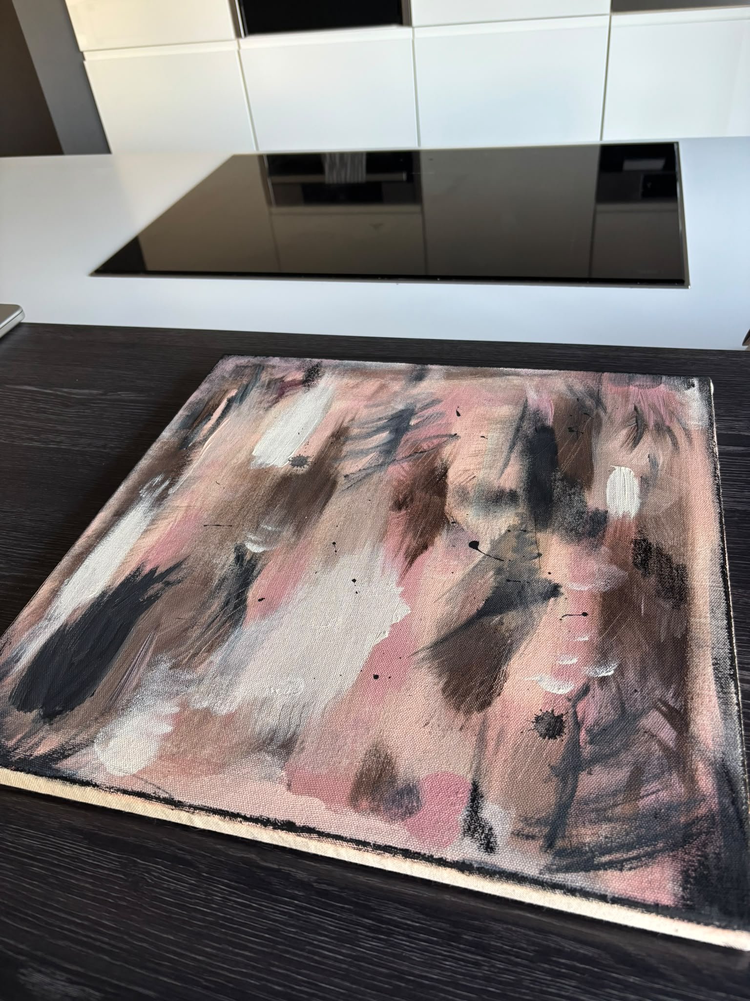 Ein abstraktes Gemälde mit Pinselstrichen in Rosa, Schwarz, Grau und Weiß, auf einem schwarzen Holztisch