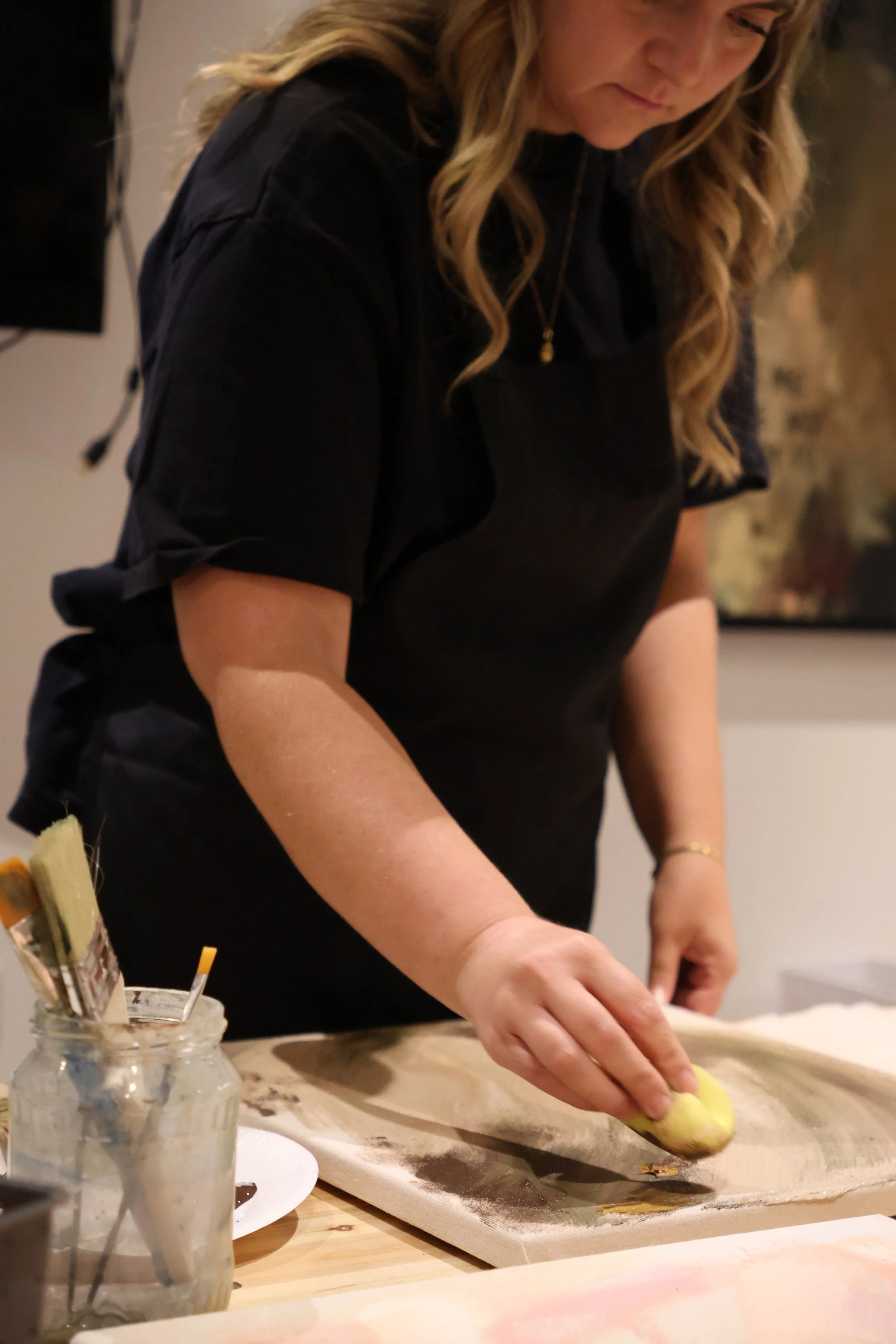 Eine Frau arbeitet an einem Küchenprojekt, sie formt oder rollt etwas auf einer Schneidmatte. Es gibt Küchenutensilien und einen Glasbehälter mit Werkzeugen auf dem Tisch.