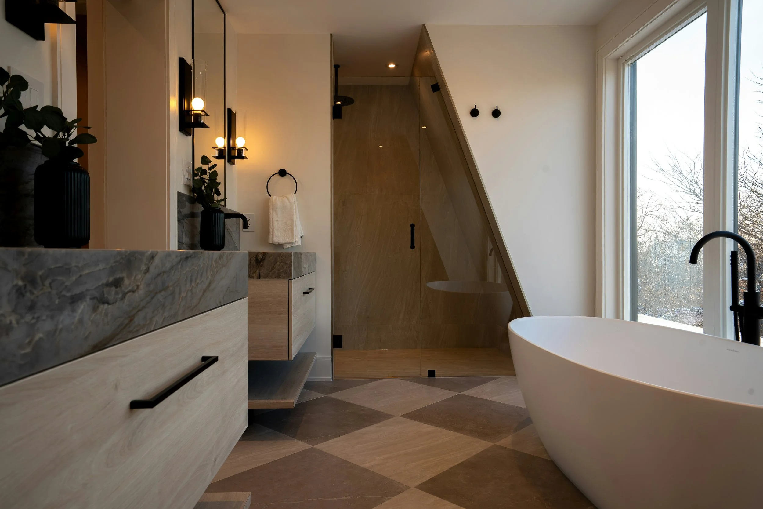 Modern bathroom with a freestanding bathtub, large window, wooden cabinets, a marble countertop, black fixtures, and decorative plants.