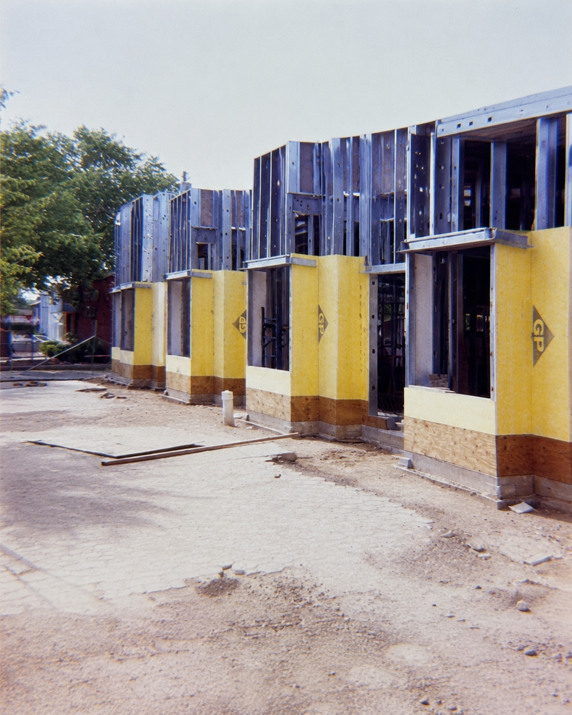 Construction site of a building with framing and partially installed yellow insulation panels, unfinished walls, and a dirt ground.