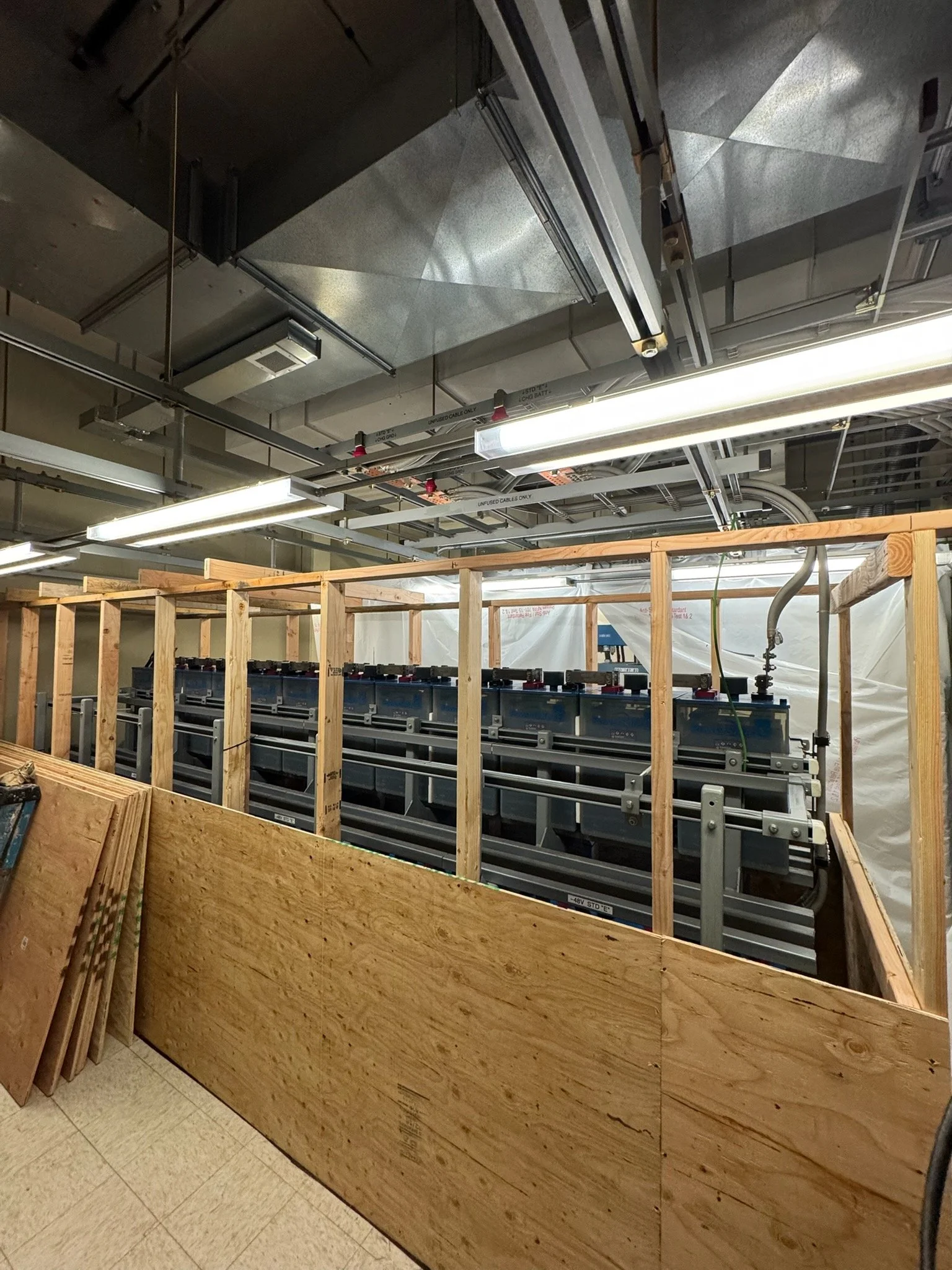Construction area with unfinished wooden framing, electrical wiring, and exposed ceiling ducts and pipes in an indoor space.