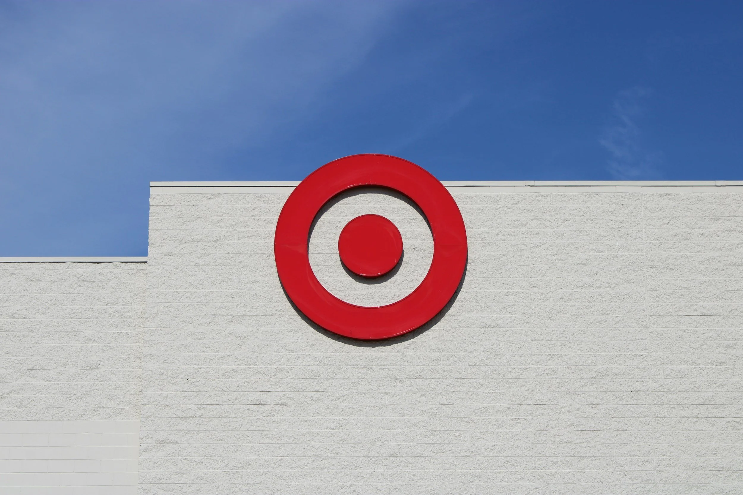 Target store logo, a red circle with a smaller red circle inside, on a white textured wall, under a blue sky.