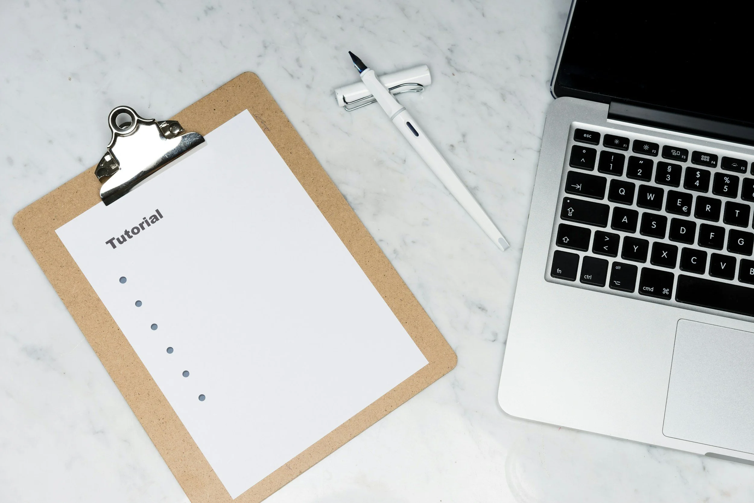 A marble desk features a clipboard with a paper titled 'Tutorial,' a white digital pen, and a laptop keyboard visible on the right side.