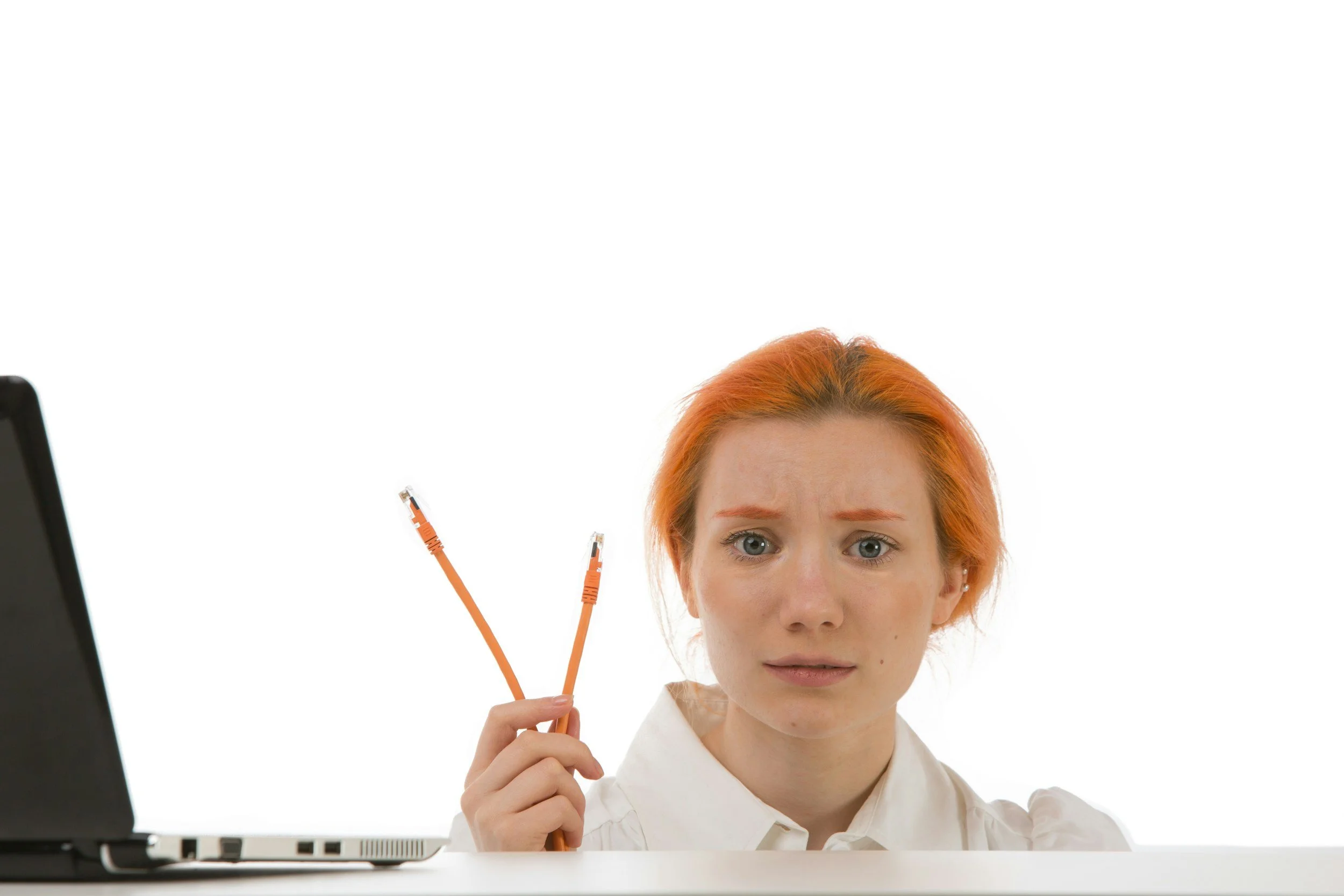 One-to- one Health and Safety Mentoring for Headteachers. A person with red hair looks puzzled while holding Ethernet cables near a laptop, with a blank white background.
