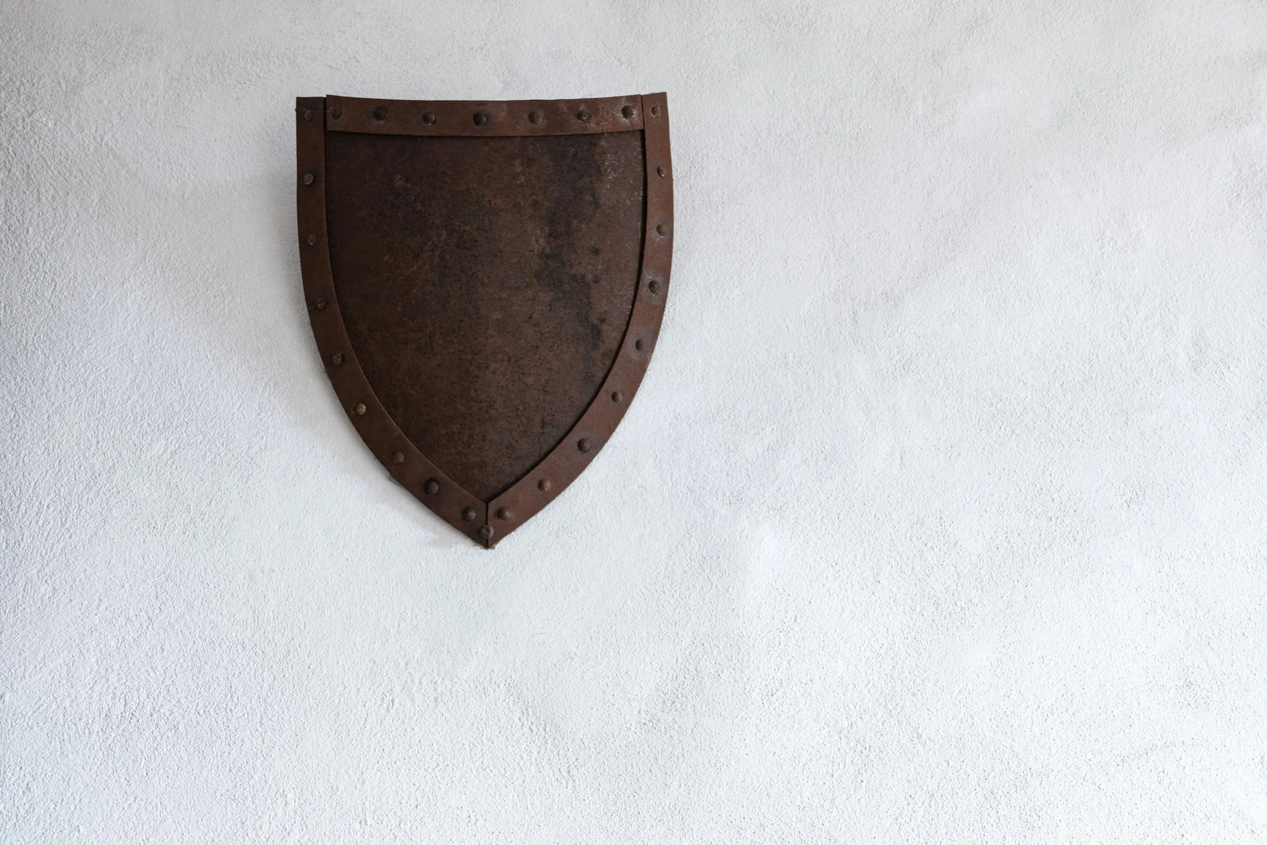 A rusted metal shield mounted on a plain white wall.