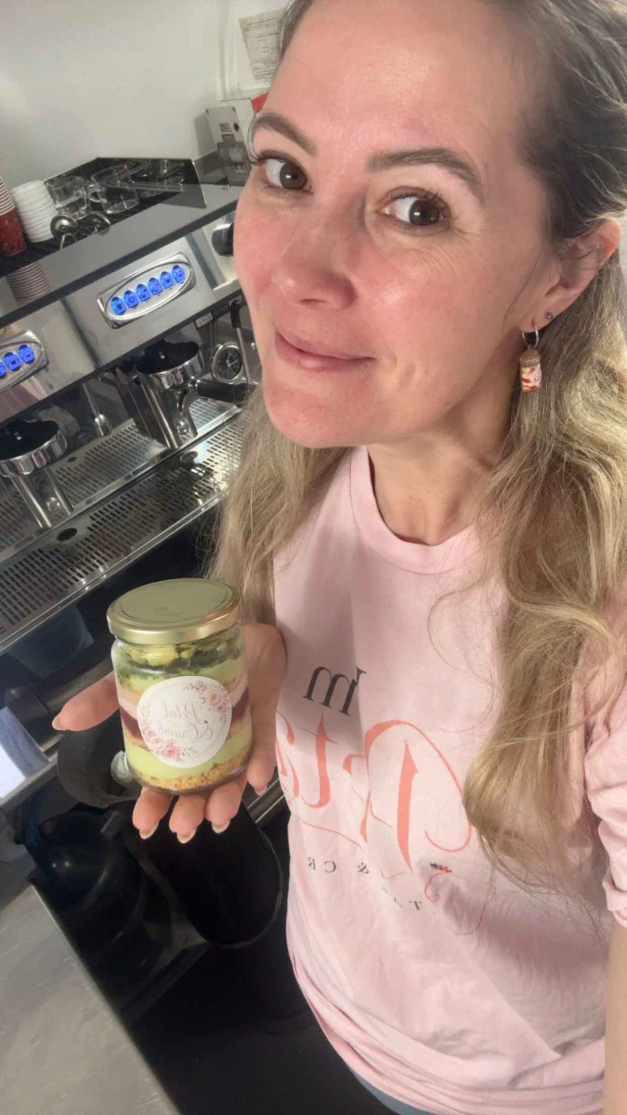 Hayley, founder of Petal & Crumb, holding  a handcrafted Matcha Meadow dessert jar beside the espresso machine in the mobile coffee trailer in Perth, Western Australia.